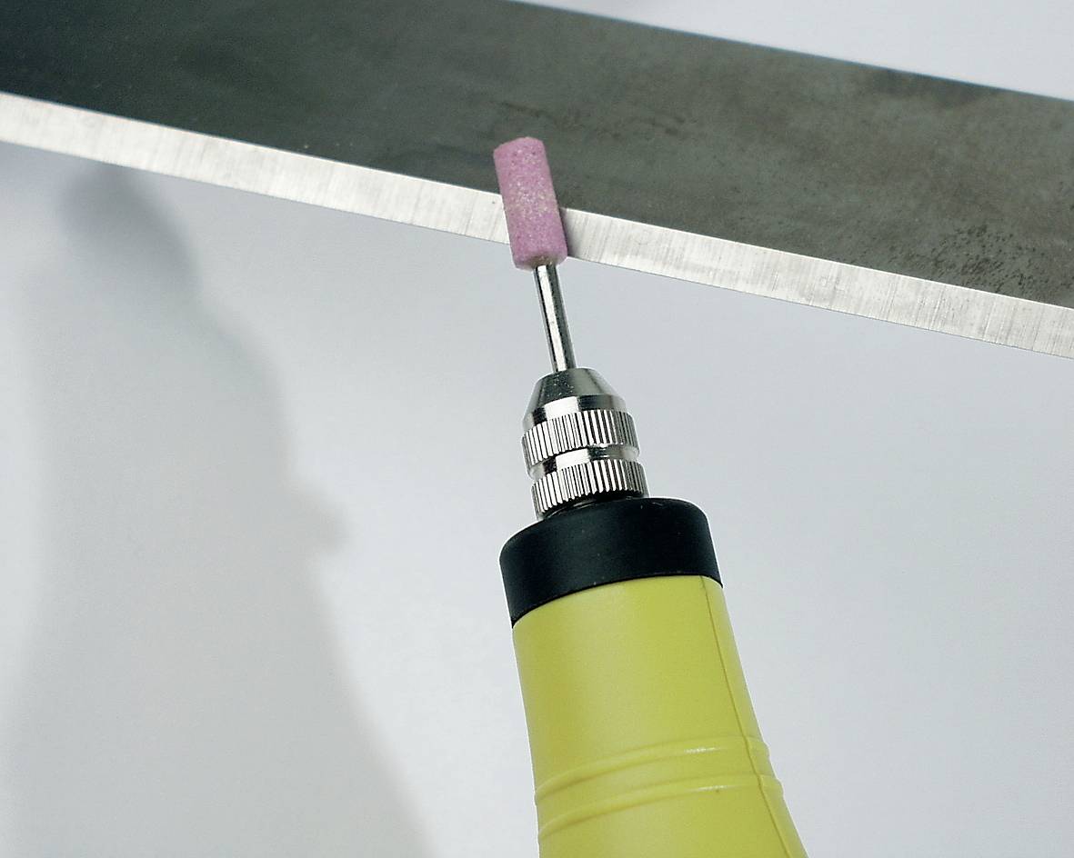 Ein gelbes Werkzeug mit einem rotierenden, rosa Schleifkopf bearbeitet die Kante eines Metallstücks.