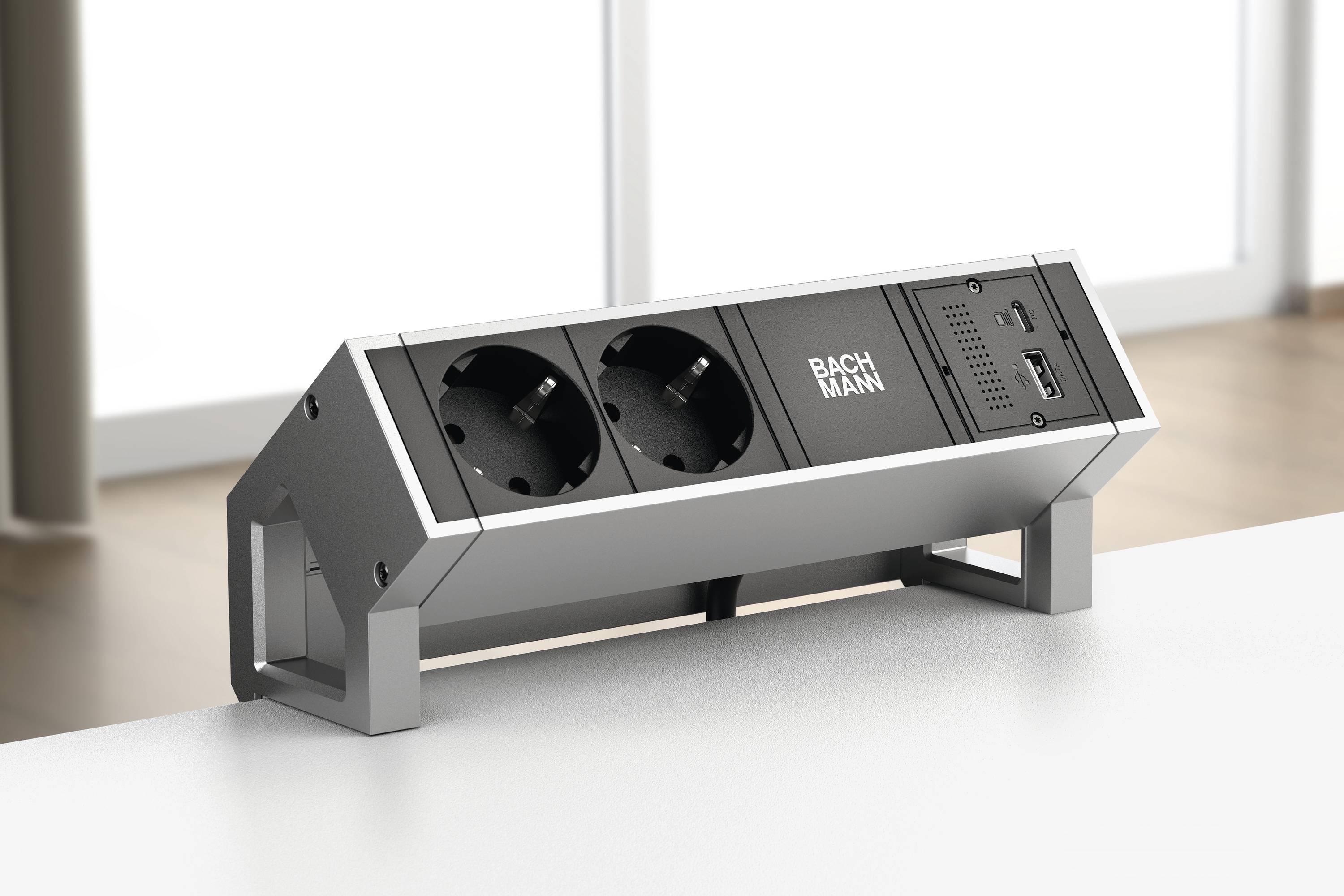 Steckdosenleiste mit zwei Schuko-Steckdosen und USB-Anschluss auf einem Tisch. Im Hintergrund Fenster mit diffusem Tageslicht.