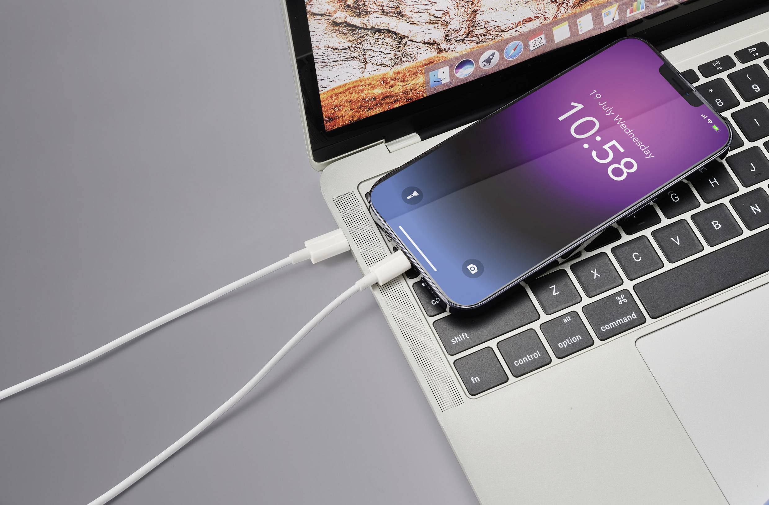 Smartphone mit violettem Bildschirm wird über ein Kabel an einen Laptop angeschlossen. Bildschirm zeigt '10:58' an.
