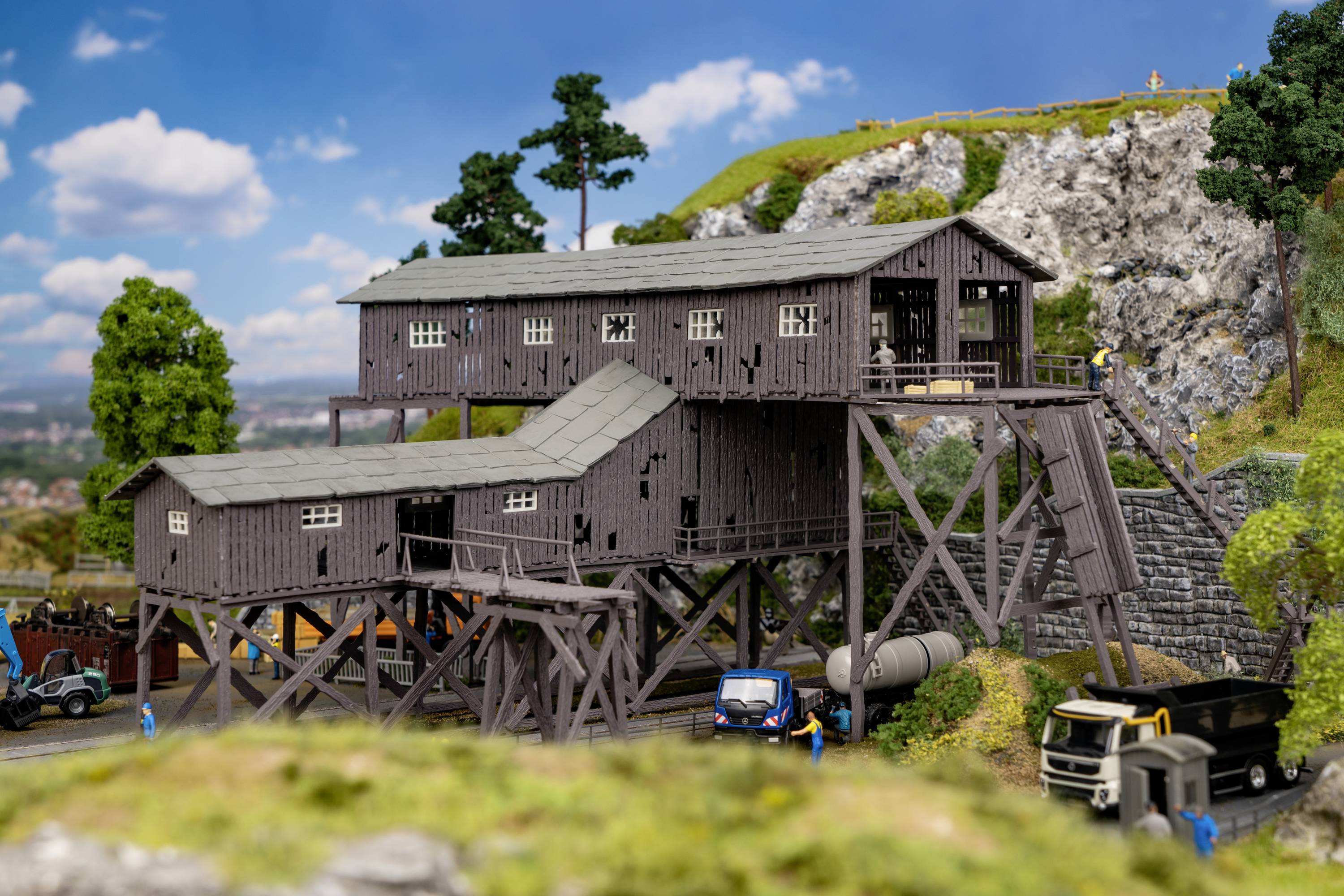 Ein Modell einer alten Bergbaustation auf einer felsigen Landschaft, umgeben von Miniaturfahrzeugen und Bäumen.