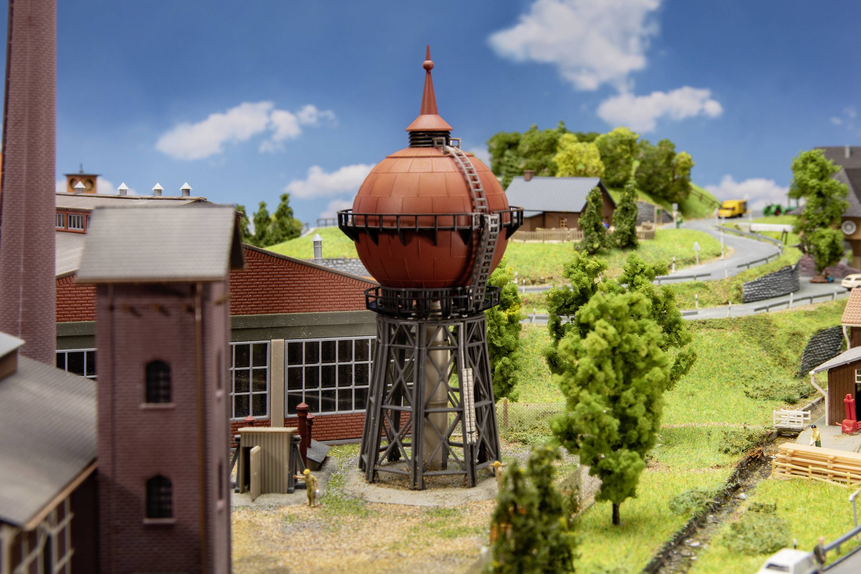 Ein Diorama zeigt eine ländliche Landschaft mit einem roten Wasserturm im Mittelpunkt, umgeben von Bäumen, Gebäuden und Straßen.