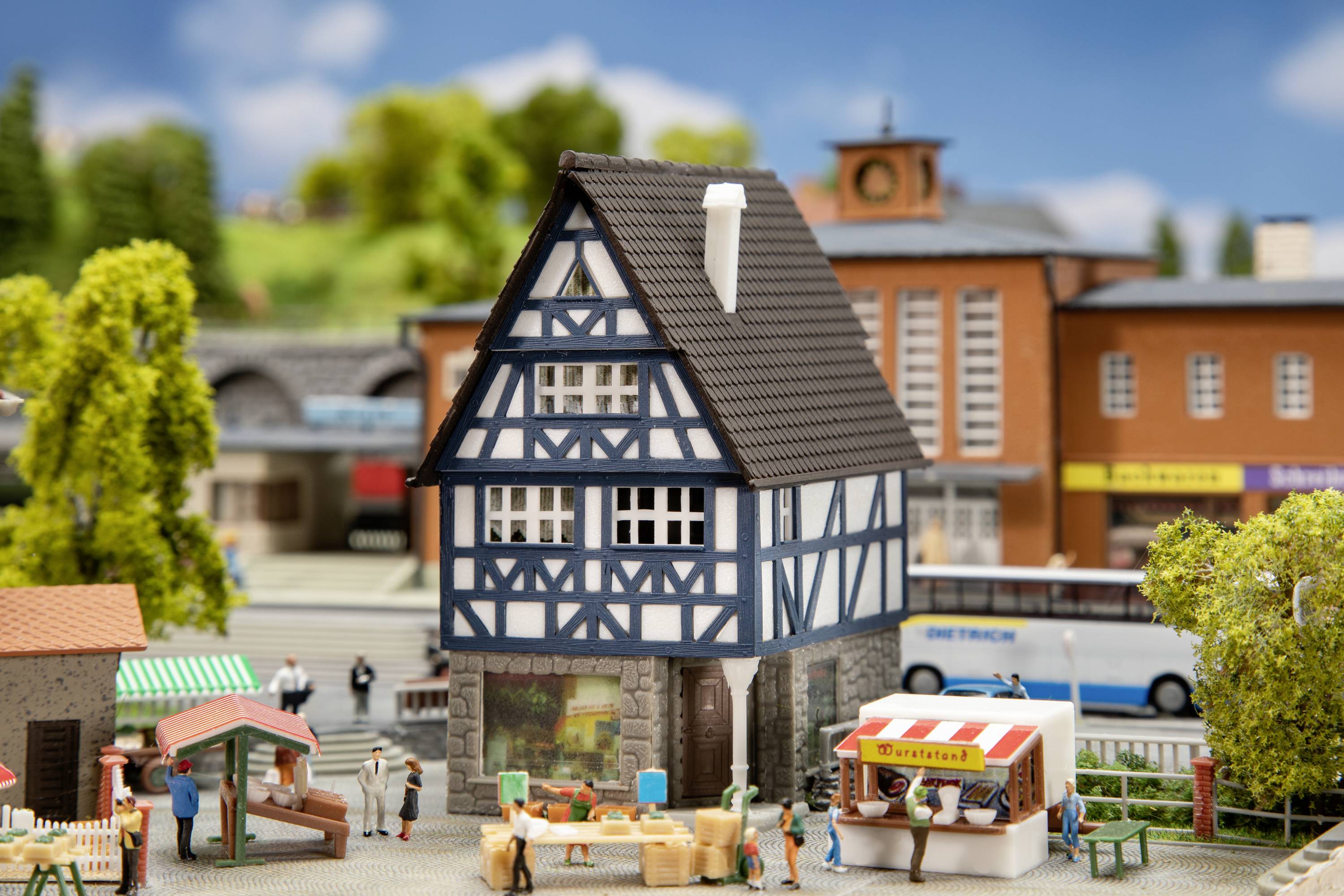 Ein Miniaturdorf mit Fachwerkhaus, Marktständen und Besuchern. Im Hintergrund sind Bäume und Gebäude sichtbar.