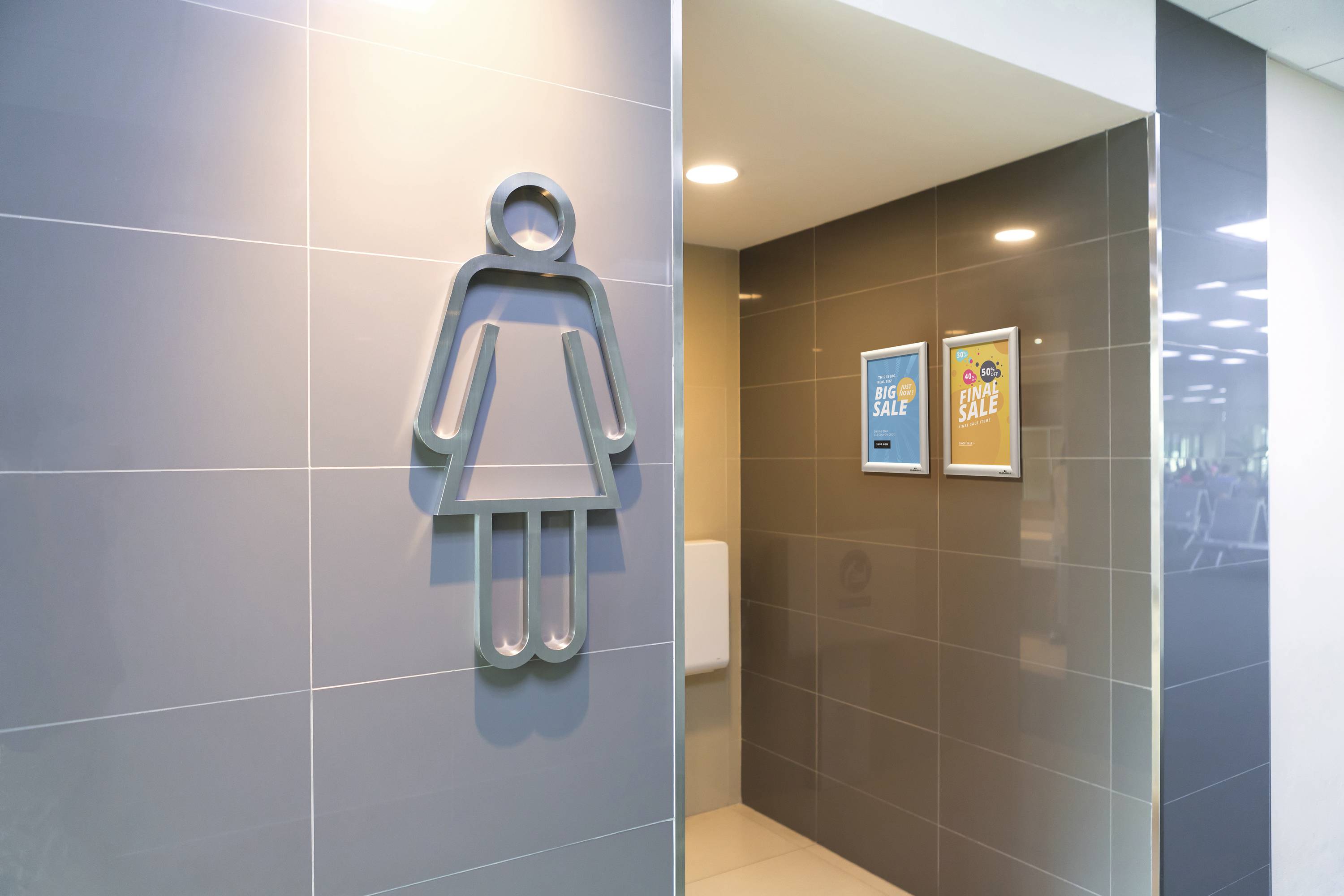 Eine Frau bedeutet das Symbol auf der Wand rechts, das einen weiblichen Toilettenbereich in einem modernen Gebäude anzeigt.