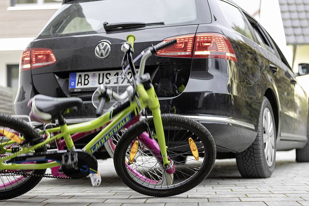 Ein Fahrrad liegt auf dem Bürgersteig hinter einem geparkten Auto. Das Fahrrad ist bunt und das Auto ist schwarz.
