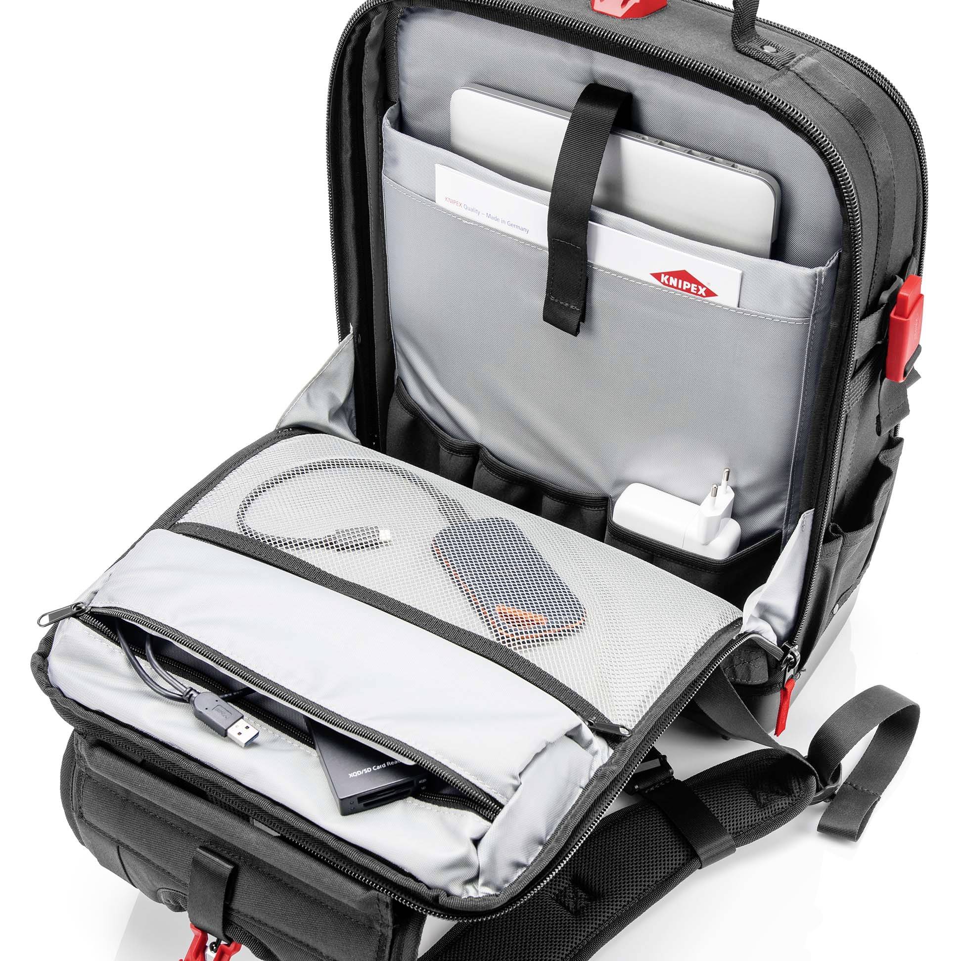 Ein offener schwarzer Rucksack zeigt Innenfächer mit einem Laptop, einer Festplatte und einem Ladekabel. Ideal für Reisen.