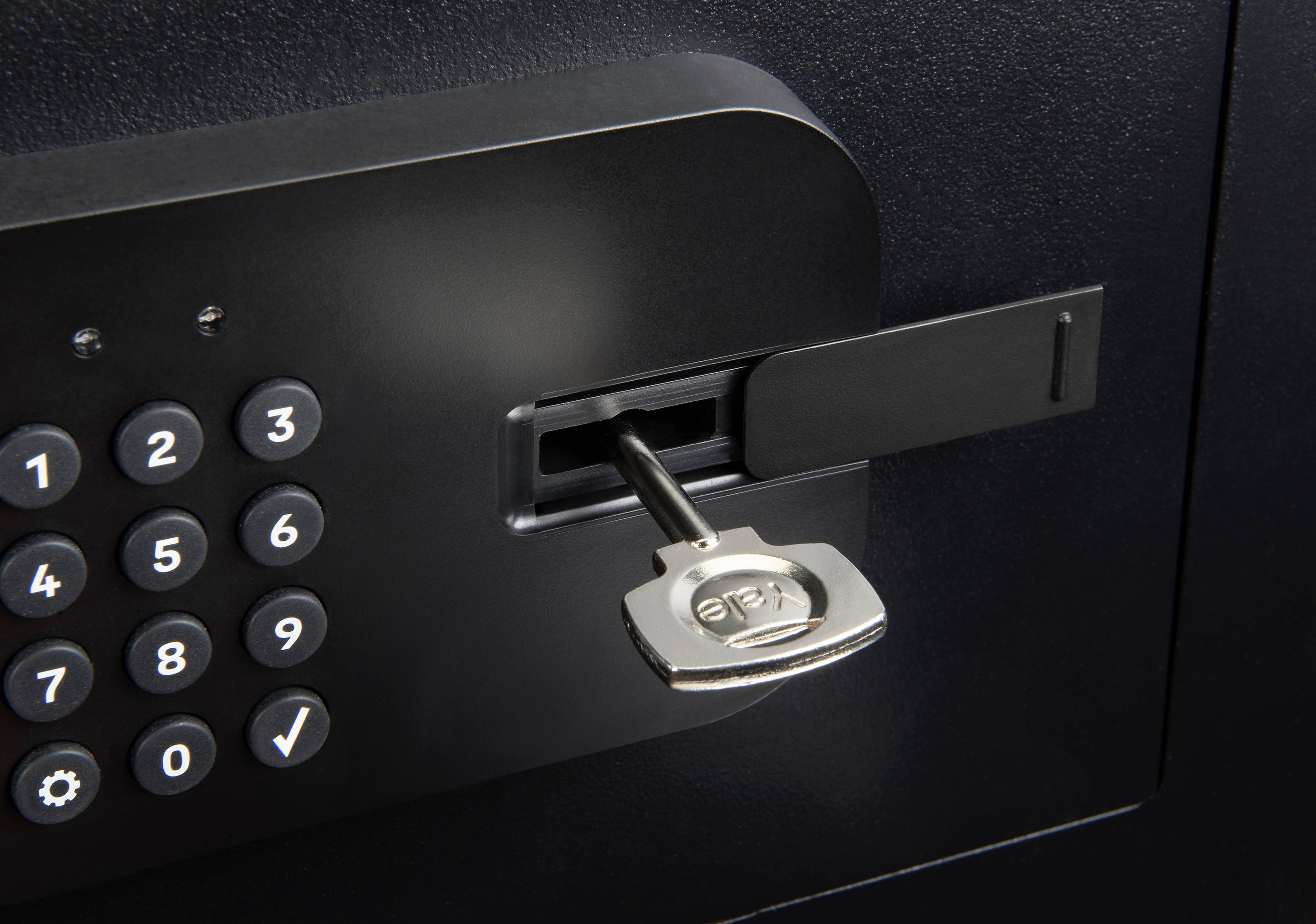 Ein Schlüssel steckt im Schloss eines modernen, schwarzen Safes mit einem digitalen Tastenfeld links daneben.