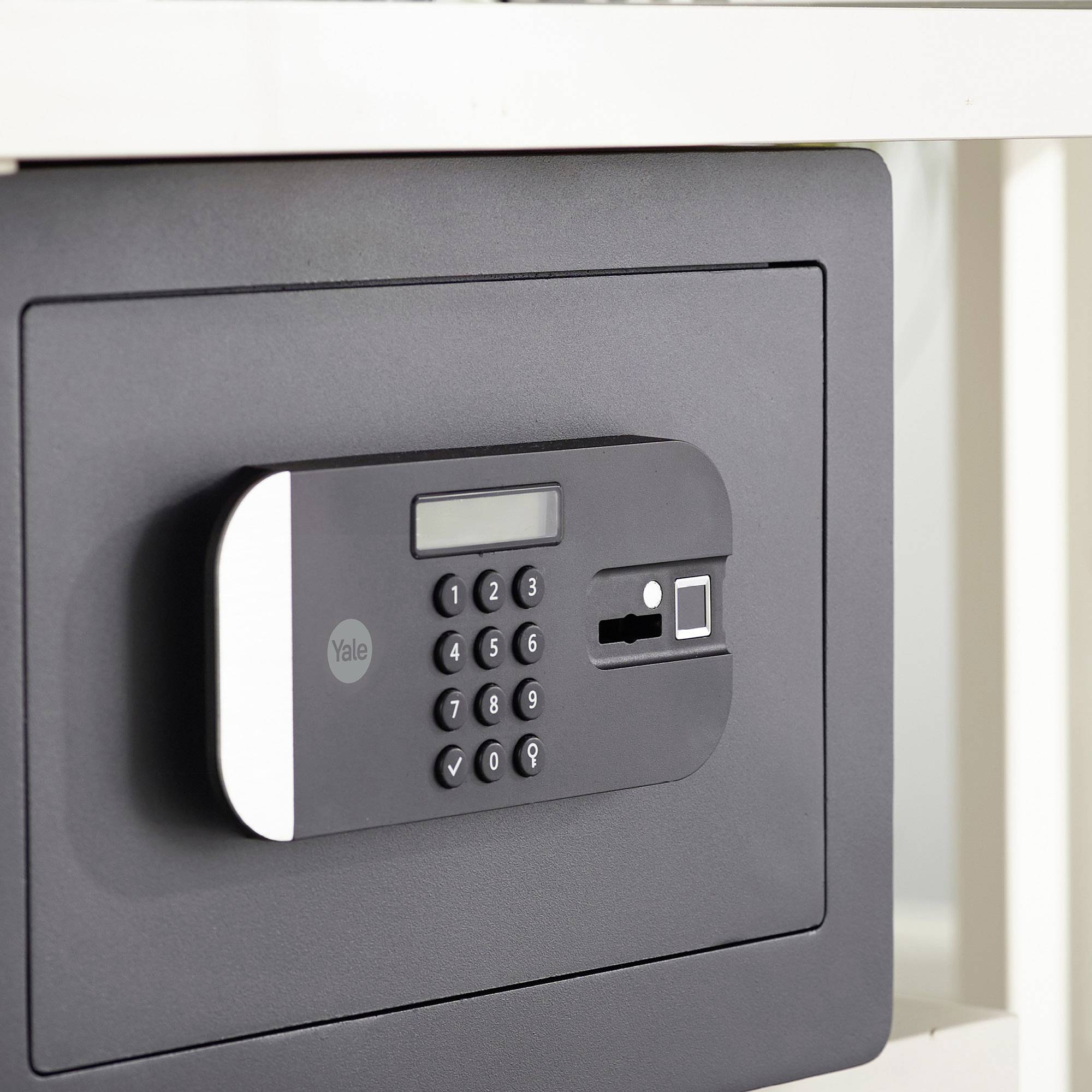 Ein grauer Safe mit Zahlencode-Tastatur und Fingerabdruckscanner an der Vorderseite, eingebaut in ein Möbelstück.