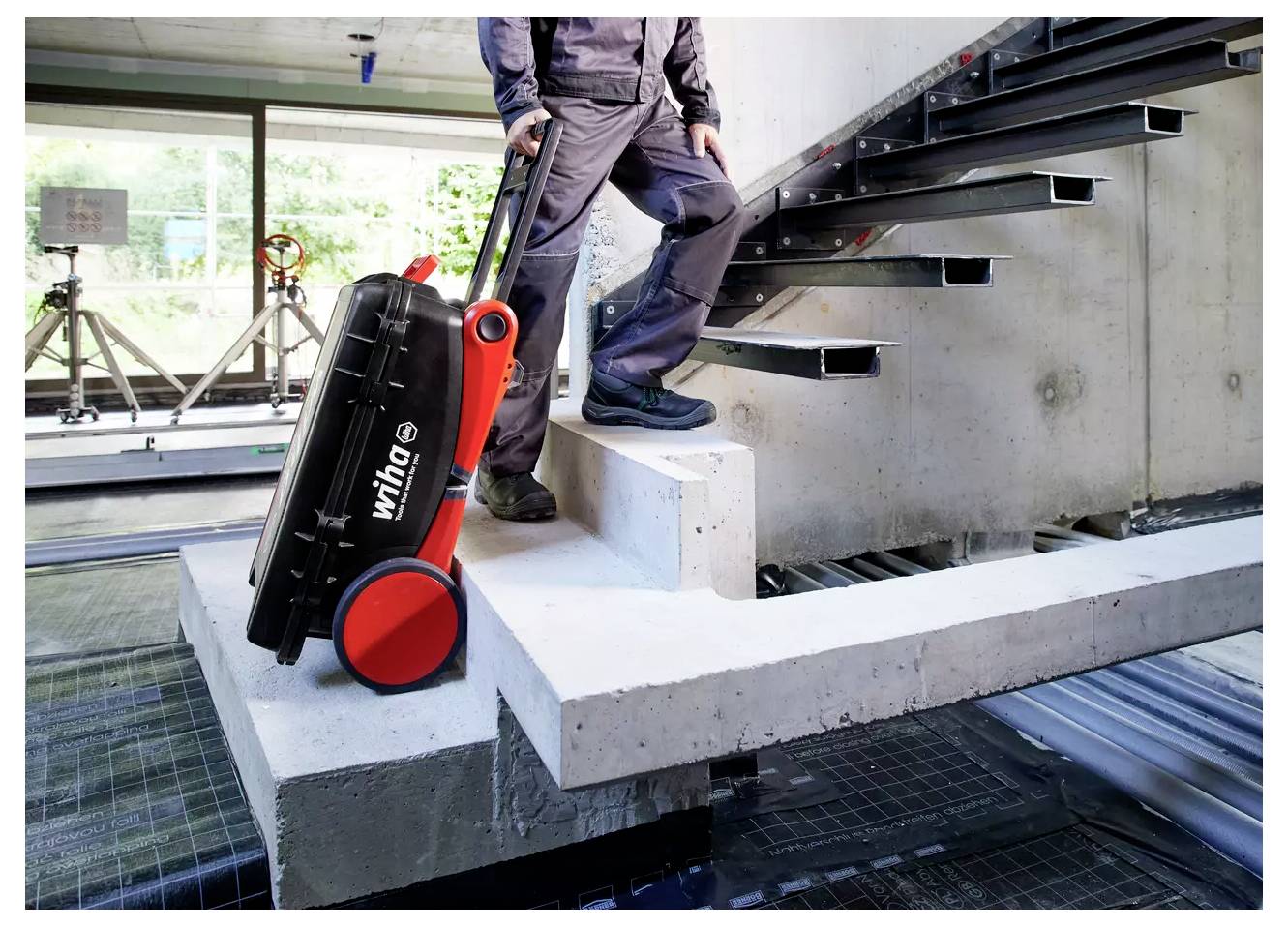 Eine Person in dunkler Arbeitskleidung nutzt einen roten zweirädrigen Sackkarre, um eine schwarze 