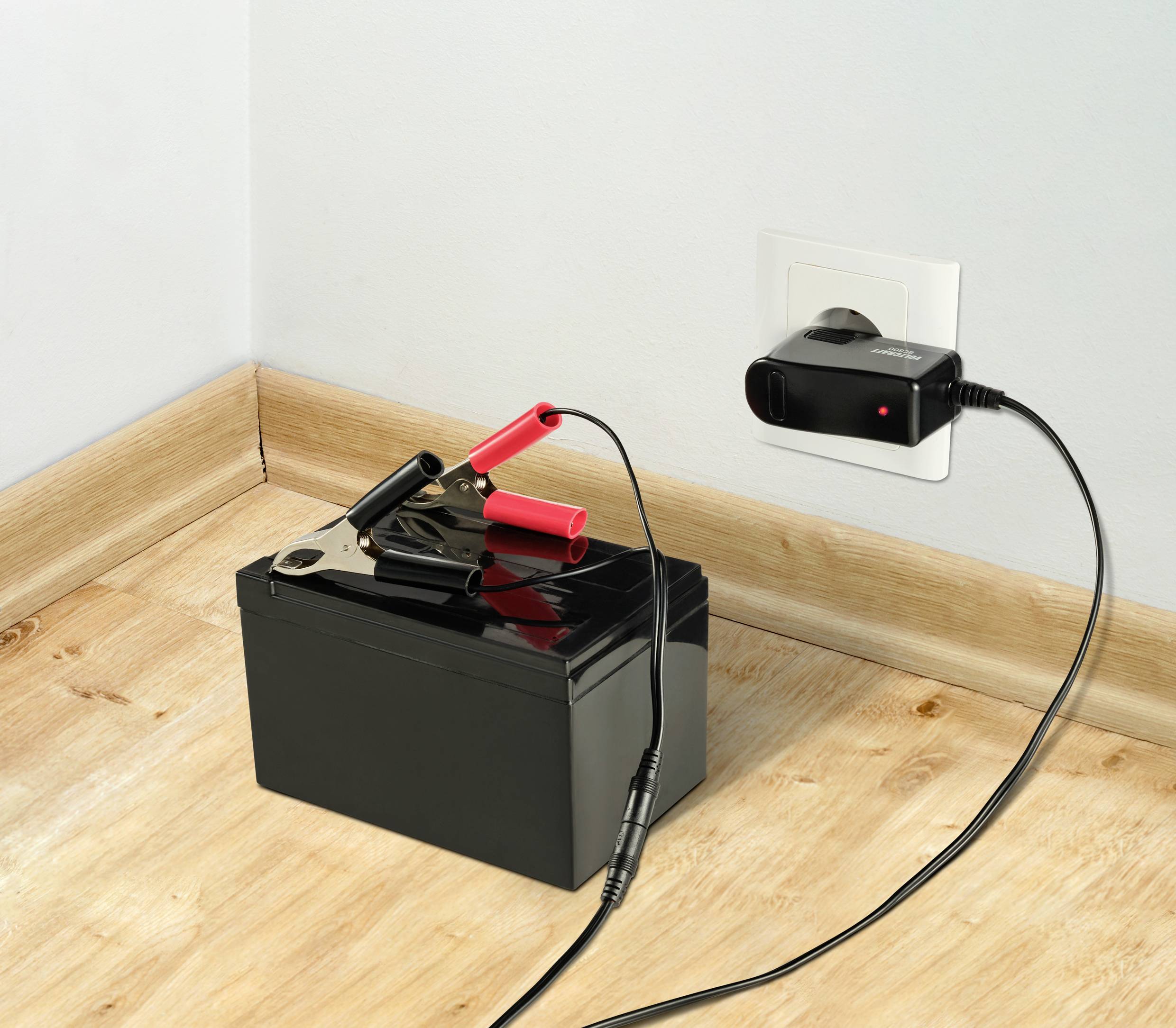 Eine Autobatterie mit angeschlossenen Klemmen wird über ein Ladegerät, das in eine Steckdose eingesteckt ist, geladen.