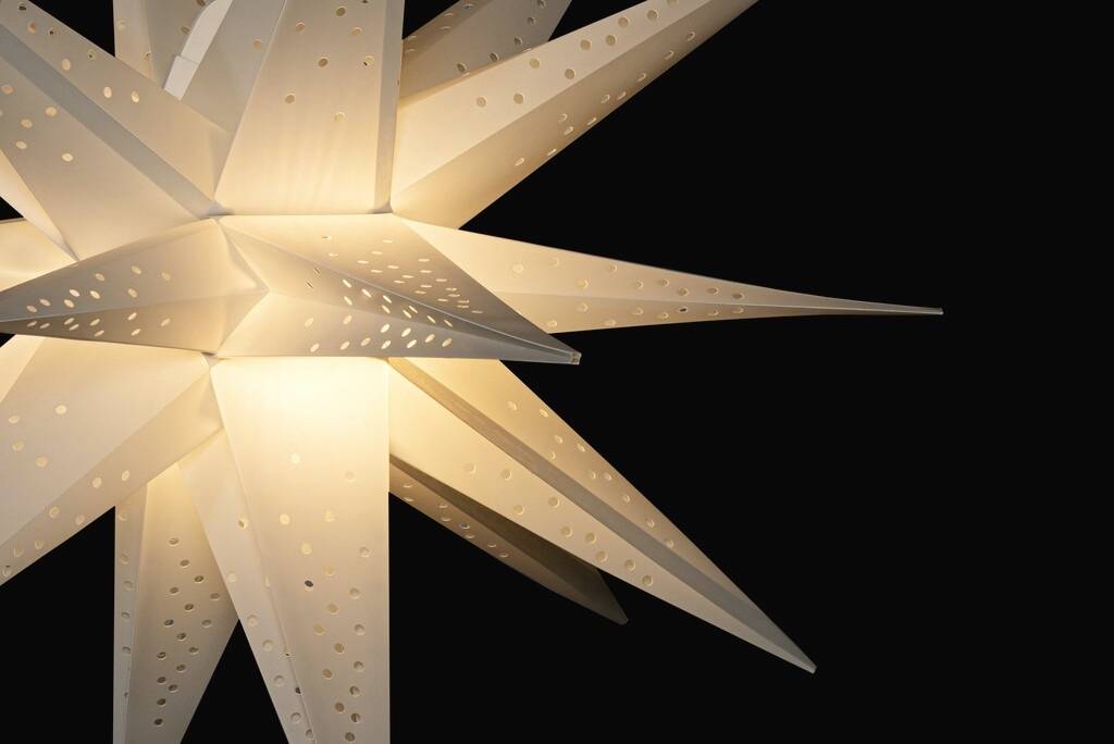 Ein beleuchteter, weißer, sternförmiger Lampenschirm vor einem schwarzen Hintergrund.