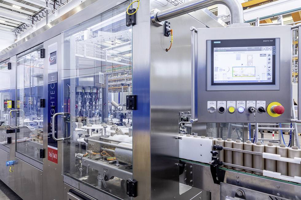Eine automatisierte Verpackungsmaschine in einer Fabrikhalle mit Steuerdisplay, klaren Schutzvorrichtungen und leeren Flaschenträgern am Band.