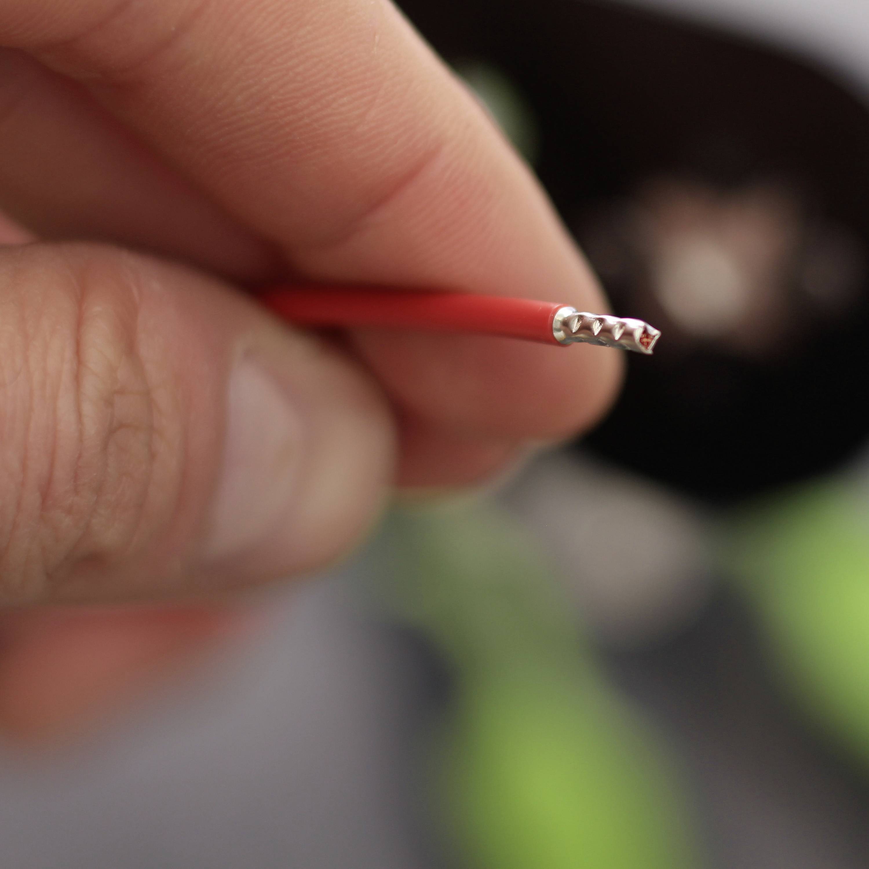 Nahaufnahme einer Hand, die ein rotes, unisoliertes Elektrokabel hält. Das Kabelende zeigt silberne Drahtenden.