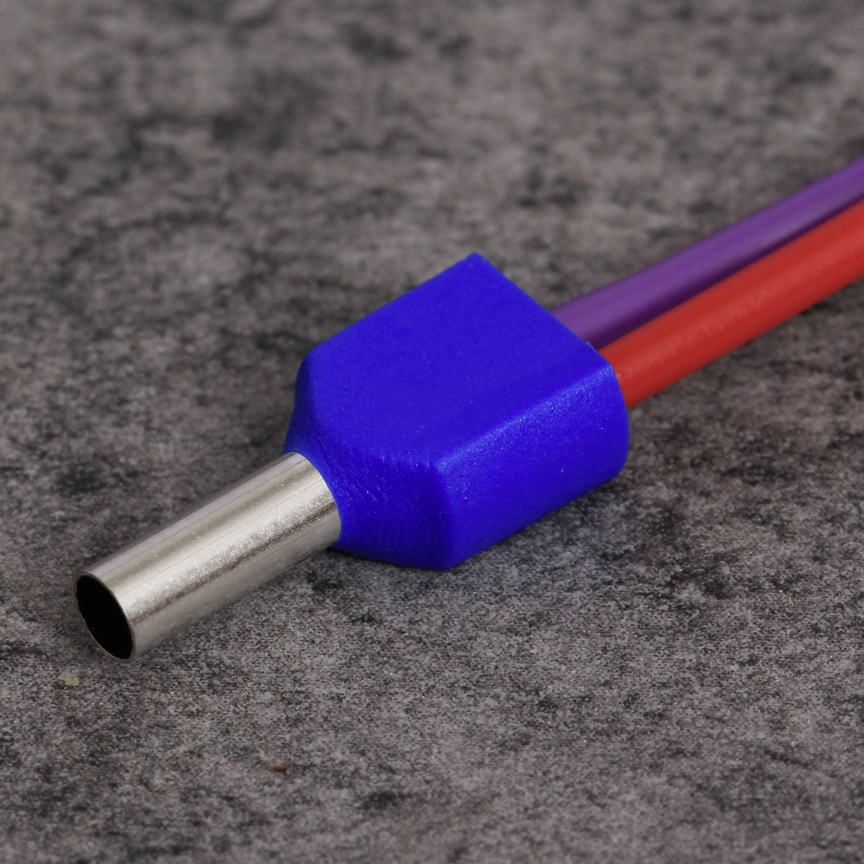 Ein blauer, metallischer Stecker mit zwei Kabeln, eines rot und eines lila, liegt auf einer grauen Oberfläche.