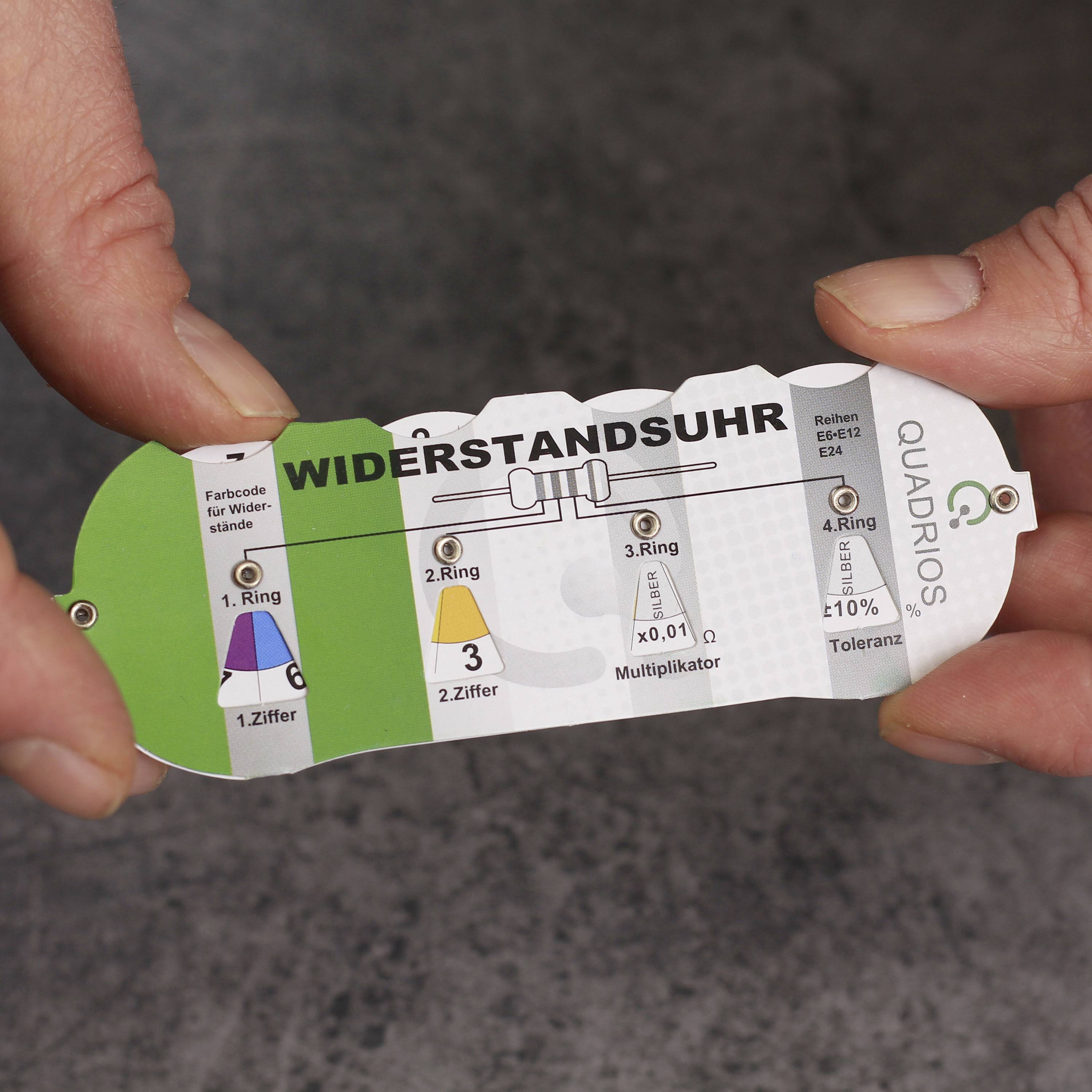 Person hält Farbcodetabelle für Widerstände mit Farbringen und Toleranzwerten. Legende erklärt Farbbedeutung für elektrische Bauteile.