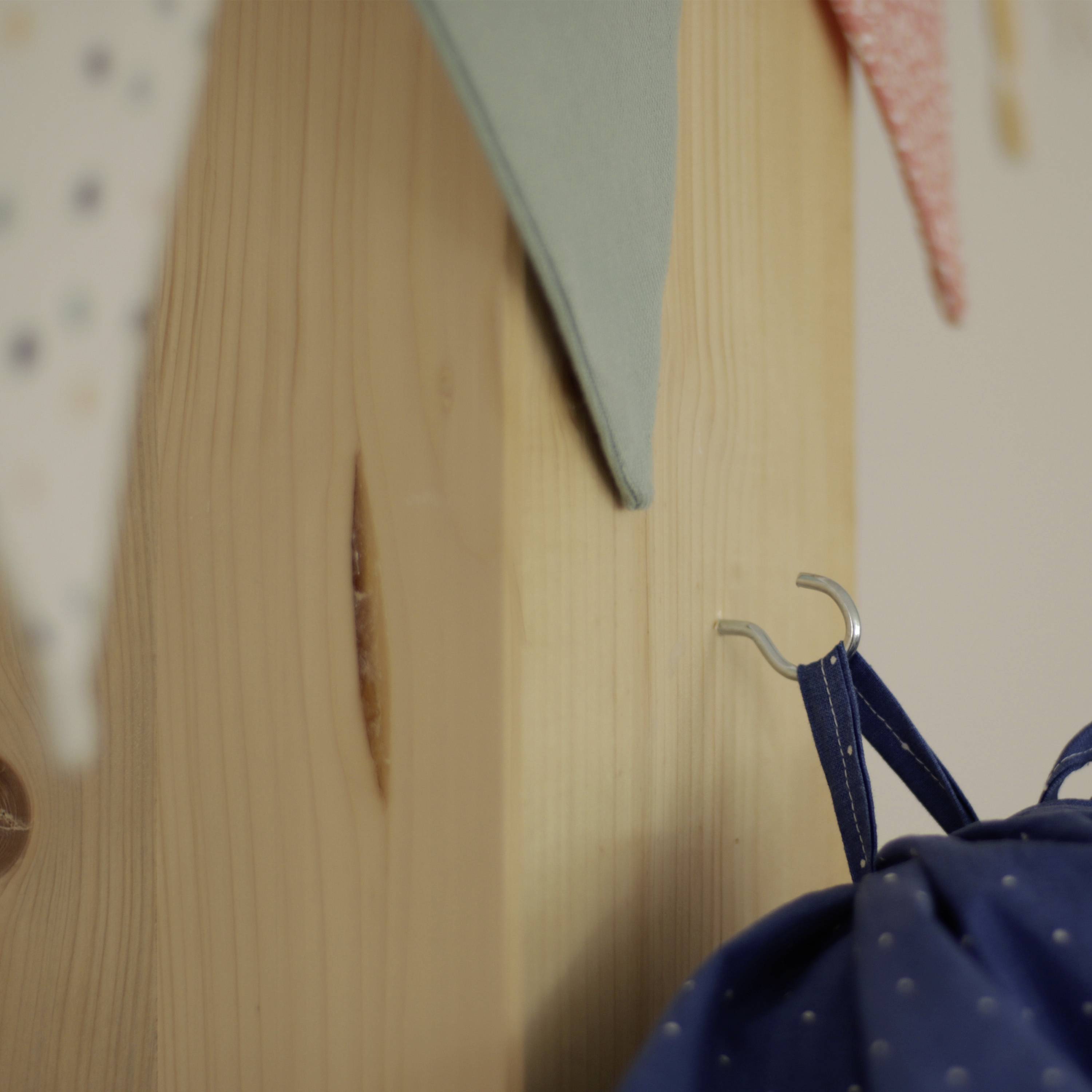 Ein blaues Tuch hängt an einem Haken an einer Holzwand; darüber bunte Stoffdreiecke als Girlande.