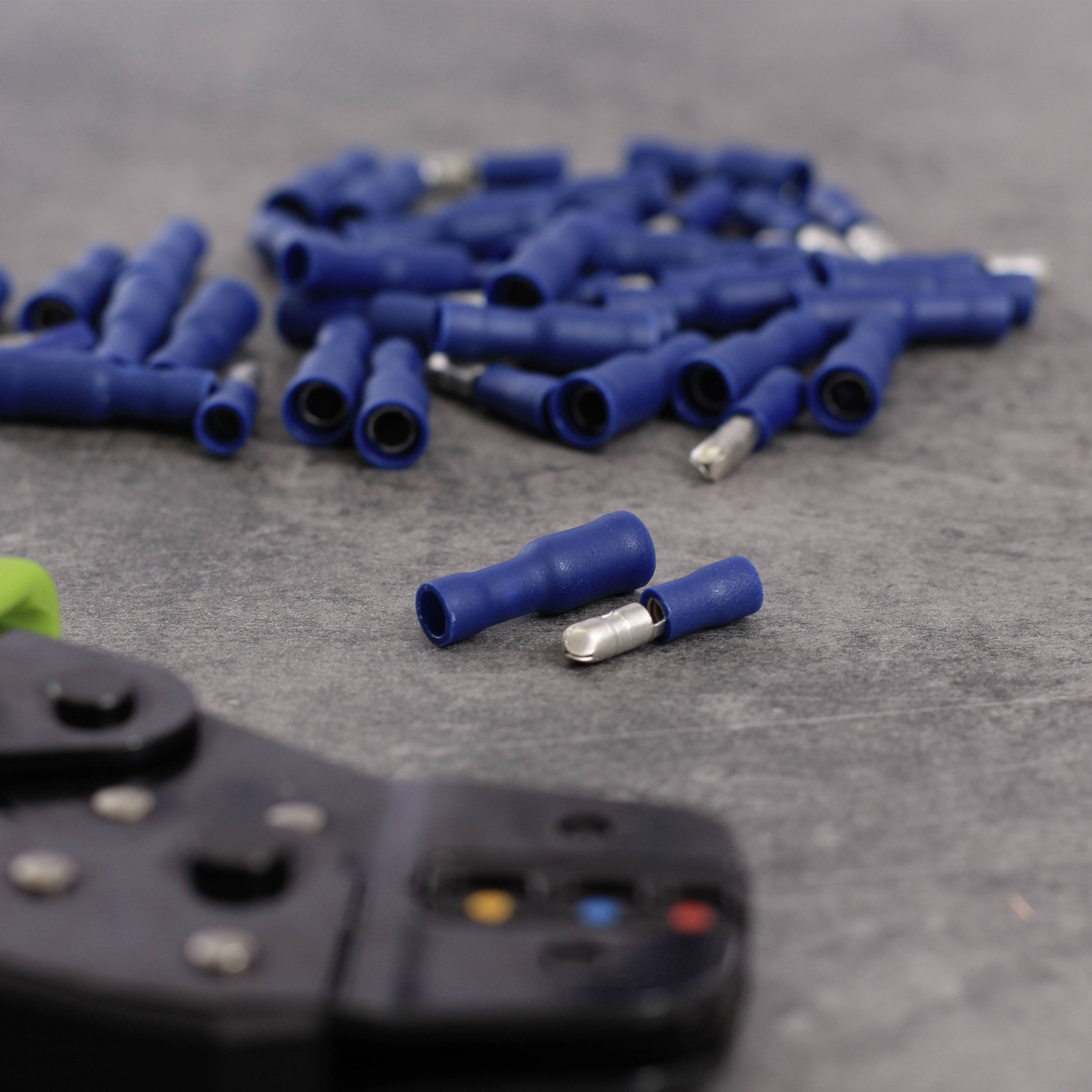 Blauer Kabelverbinder und Crimpzange auf grauem Hintergrund. Viele Verbinder sind verstreut, ein Verbinder und Zange im Vordergrund.