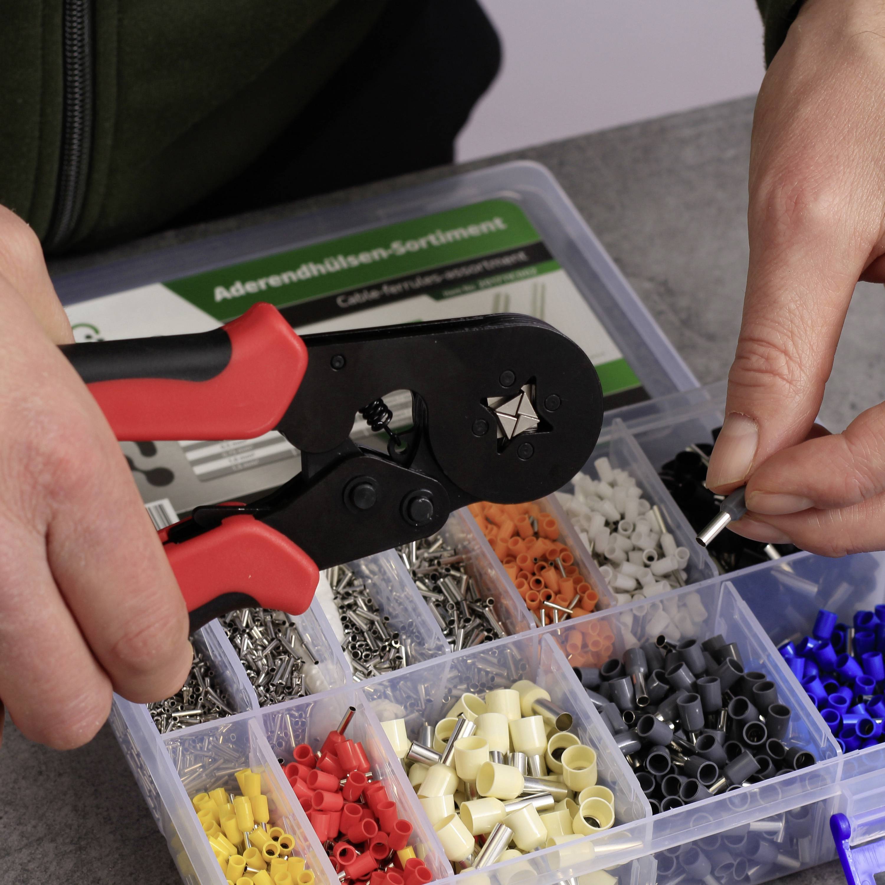 Hand crimping tool zum Crimpen von Kabeln mit Crimpeinsätzen in verschiedenen Farben und Größen. Nahaufnahme auf einem Tisch.