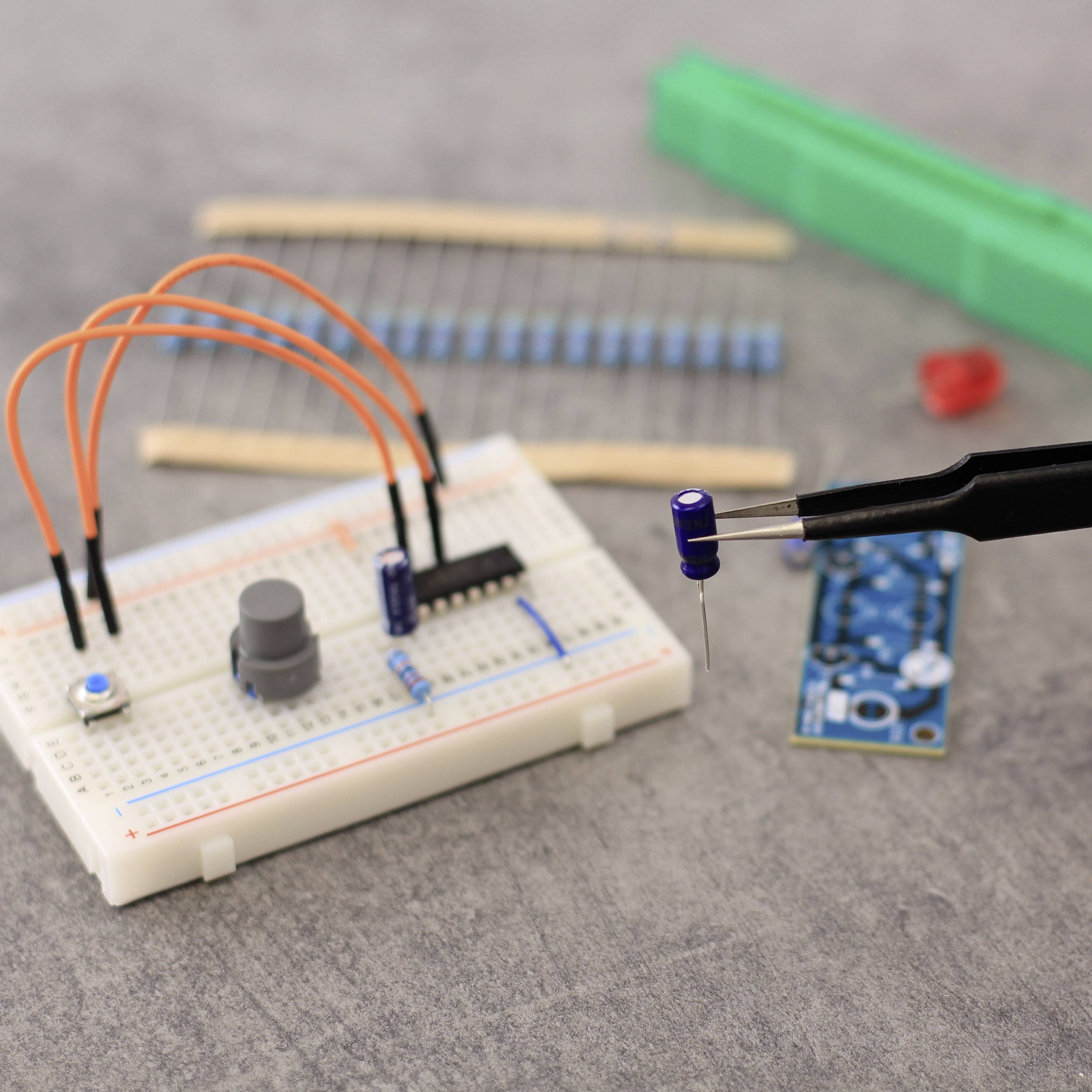 Elektronikaufbau mit Steckbrett, Widerständen, Kondensator und Sensor. Lötkolben mit blauer Spitze in Nahaufnahme.