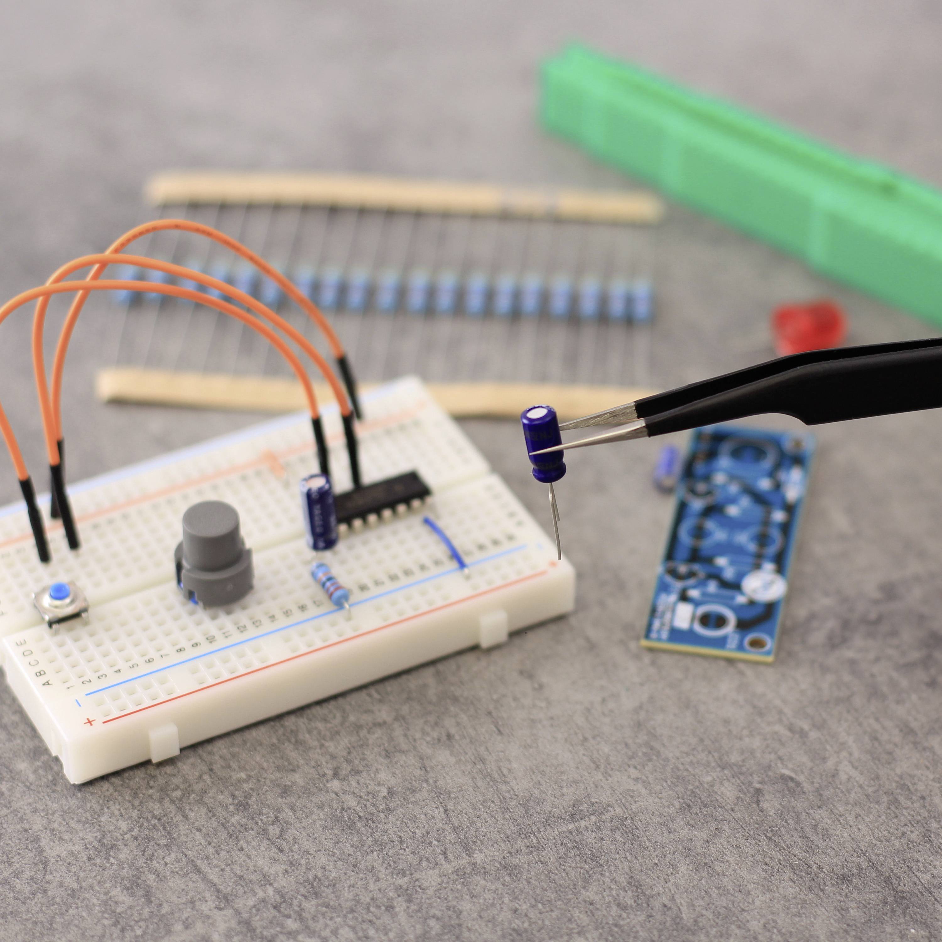 Lötstation mit Schaltbrett, Kondensatoren und Widerständen, ideal für Elektronikprojekte. Hintergrund: graue Oberfläche.