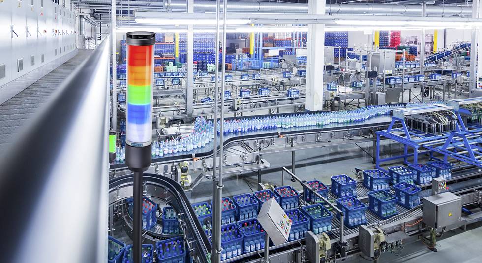 Produktionsanlage in einer Fabrik mit automatisierten Fließbändern für Flaschen. Im Vordergrund ist eine mehrfarbige Signalleuchte zu sehen.