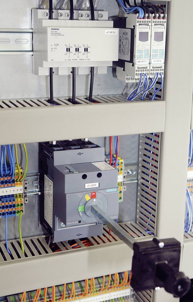 Ein Schaltschrank mit elektrischen Komponenten und farbig verkabelten Verbindungen. Im Mittelpunkt steht ein großer Schalter.