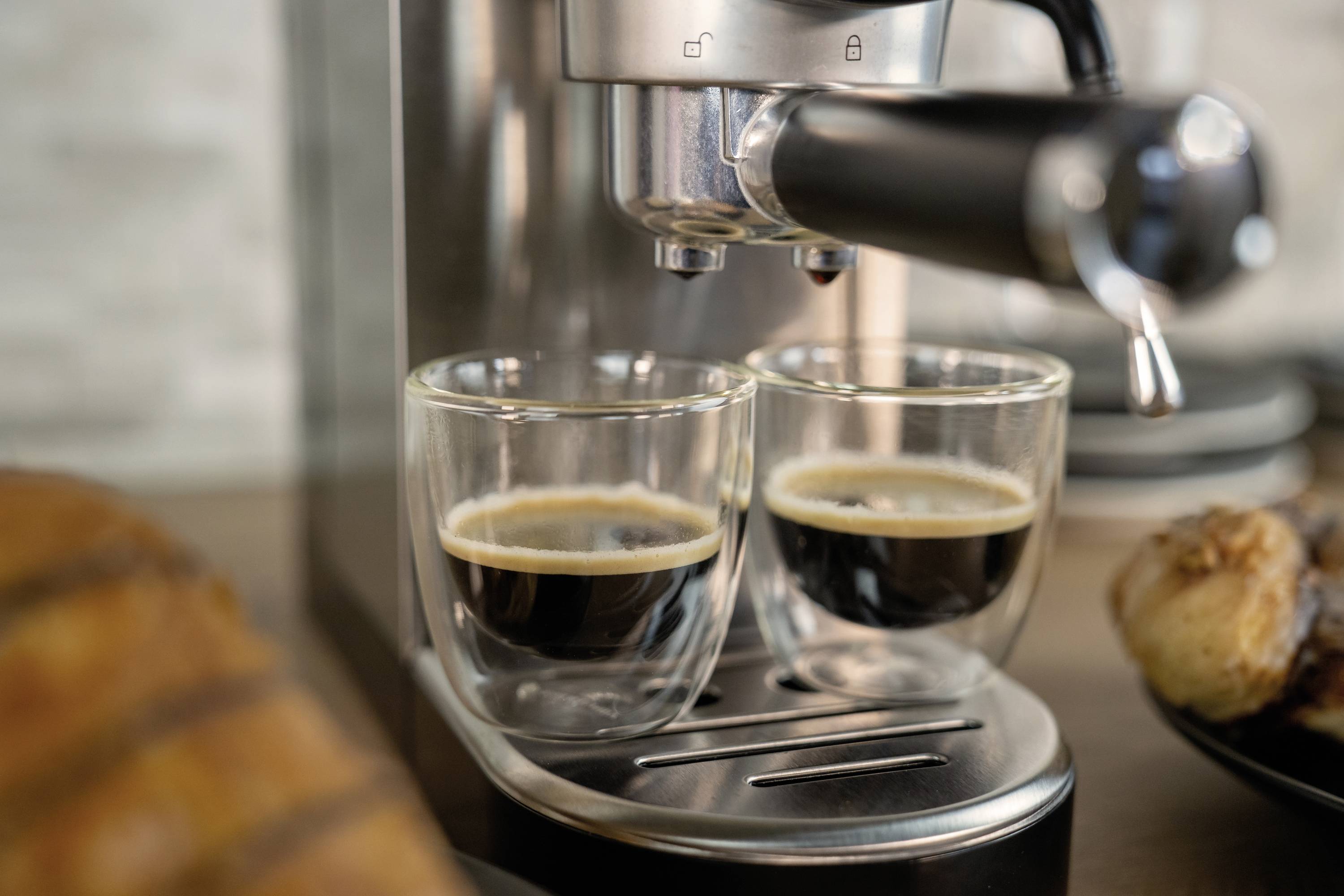 Espressomaschine, die zwei Tassen Espresso gleichzeitig zubereitet, im Vordergrund sind Teller mit Gebäck.
