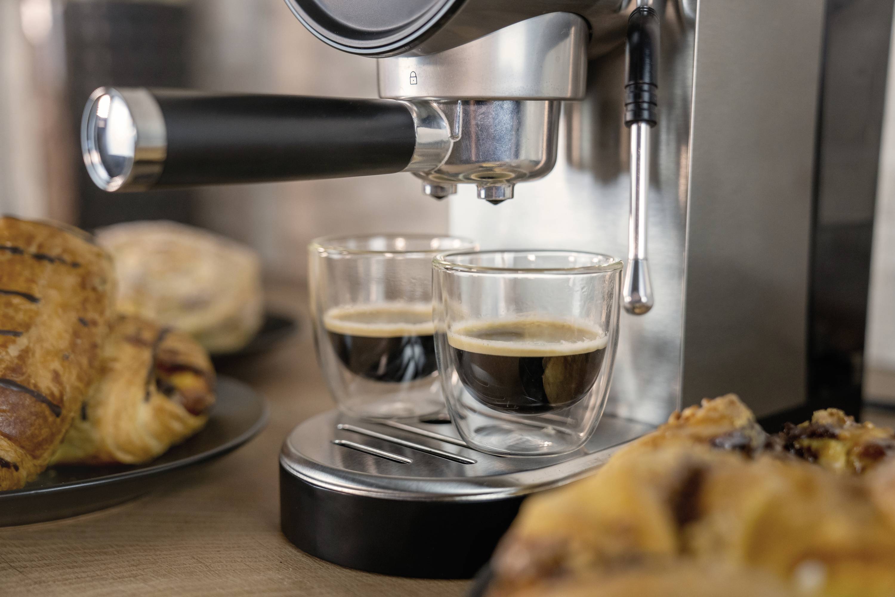 Espressomaschine brüht zwei Tassen Kaffee, von Gebäck umgeben.