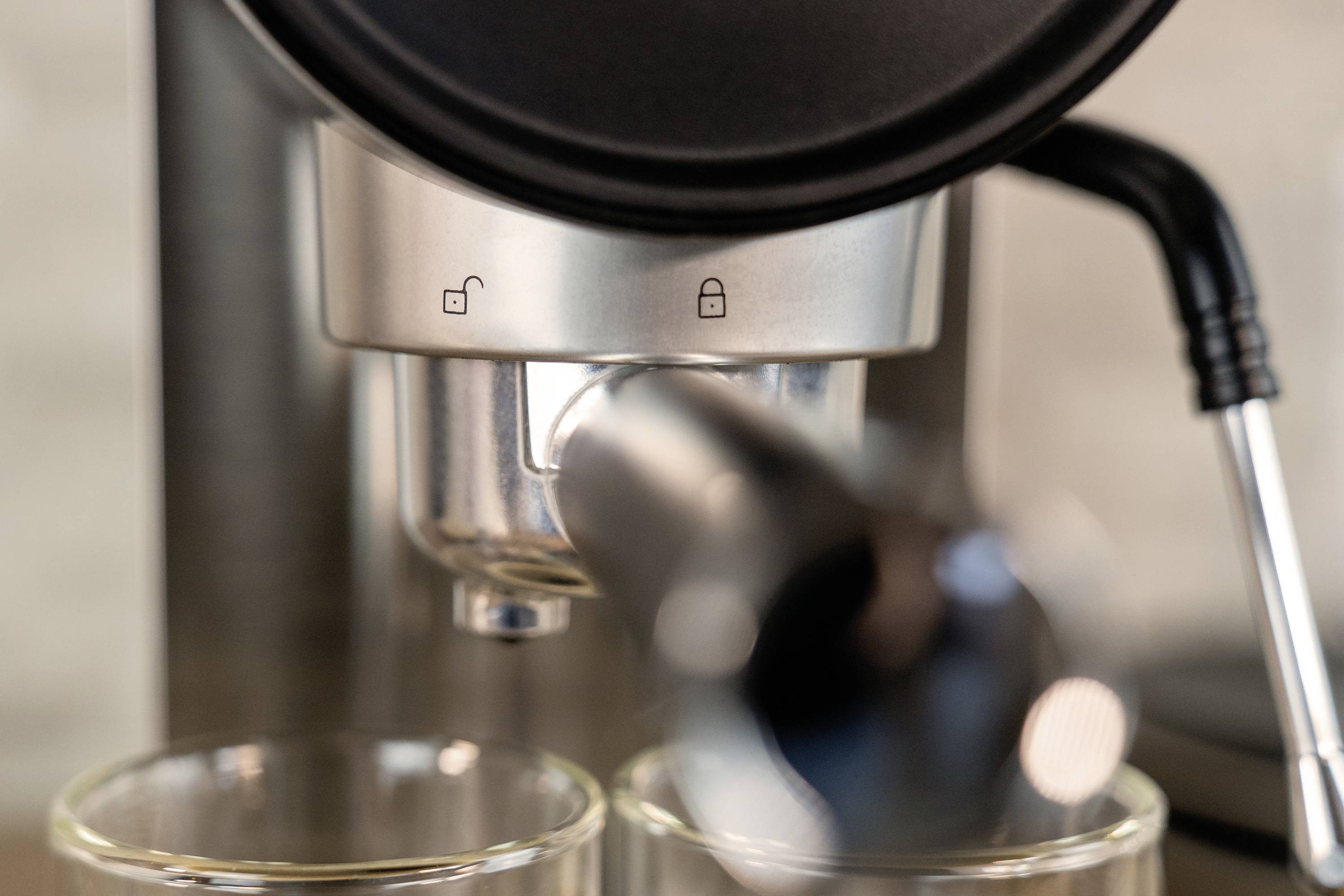 Nahaufnahme einer Espressomaschine mit herausfließendem Kaffee in zwei Gläser. Symbole zeigen, ob die Maschine verriegelt ist.