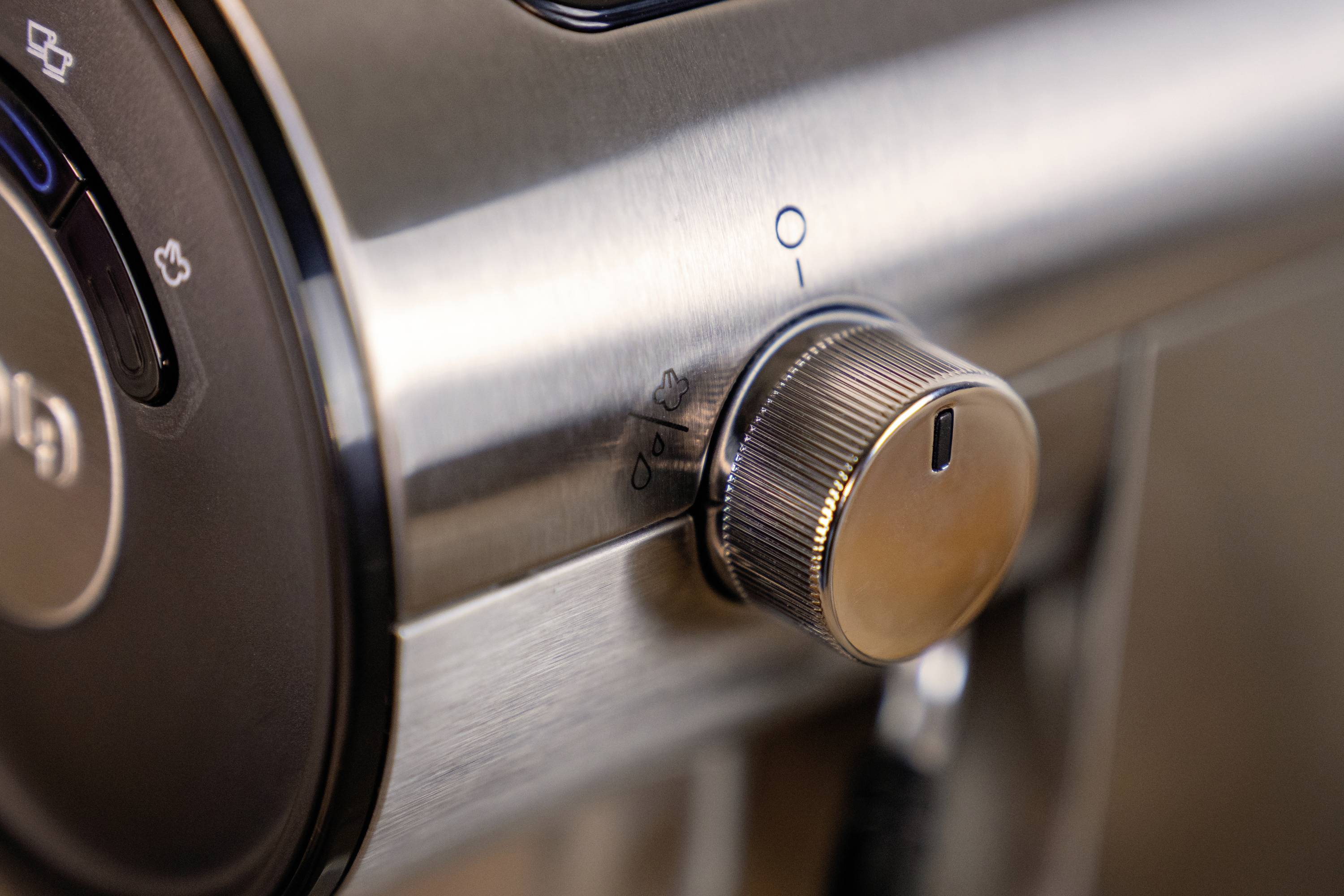 Ein glänzender Metallknopf an einem Elektrogerät, mit Markierungen der Einstellungen für Ein und Aus. Tasten neben dem Knopf sind sichtbar.