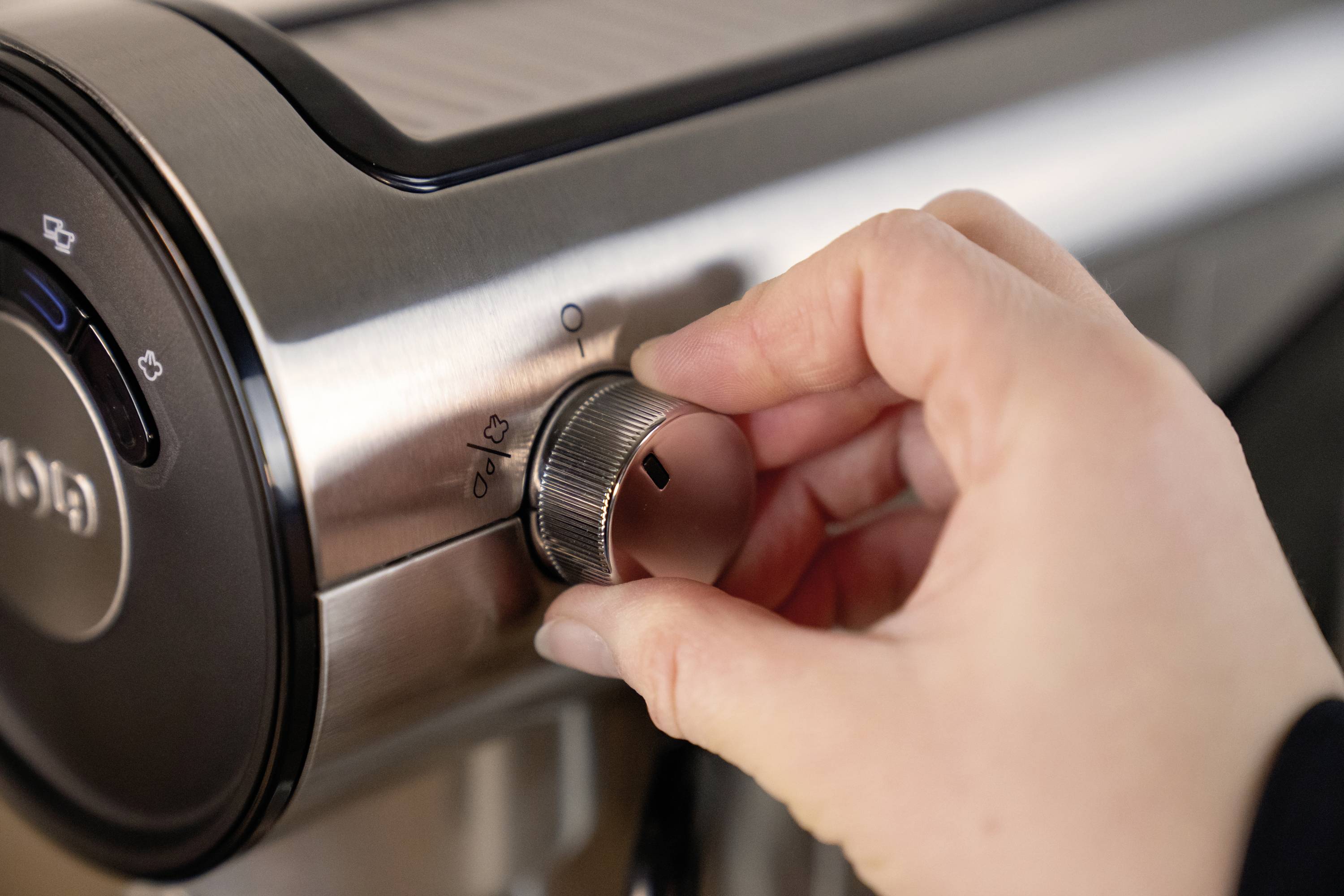 Eine Hand dreht den Knopf einer Kaffeemaschine, um den Mahlgrad einzustellen.