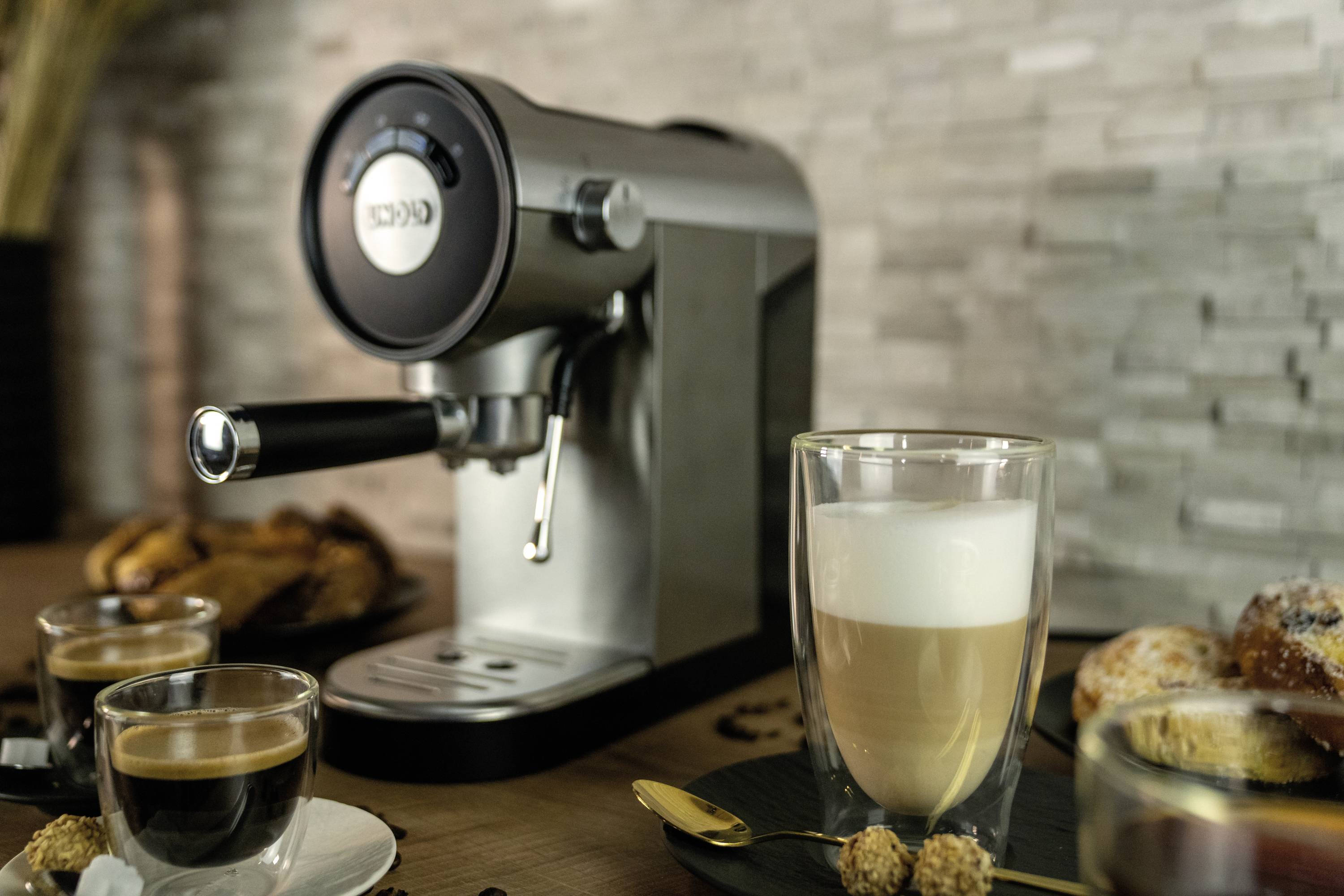 Espressomaschine auf Holzoberfläche, umgeben von verschiedenen Kaffeetassen und Gebäck in einem gemütlichen Setting.