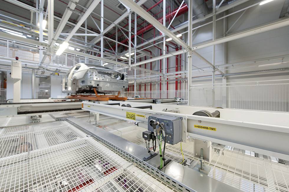 Ein Auto wird in einer Fabrik auf einer Förderanlage bewegt, umgeben von Stahlträgern und industriellem Interieur.