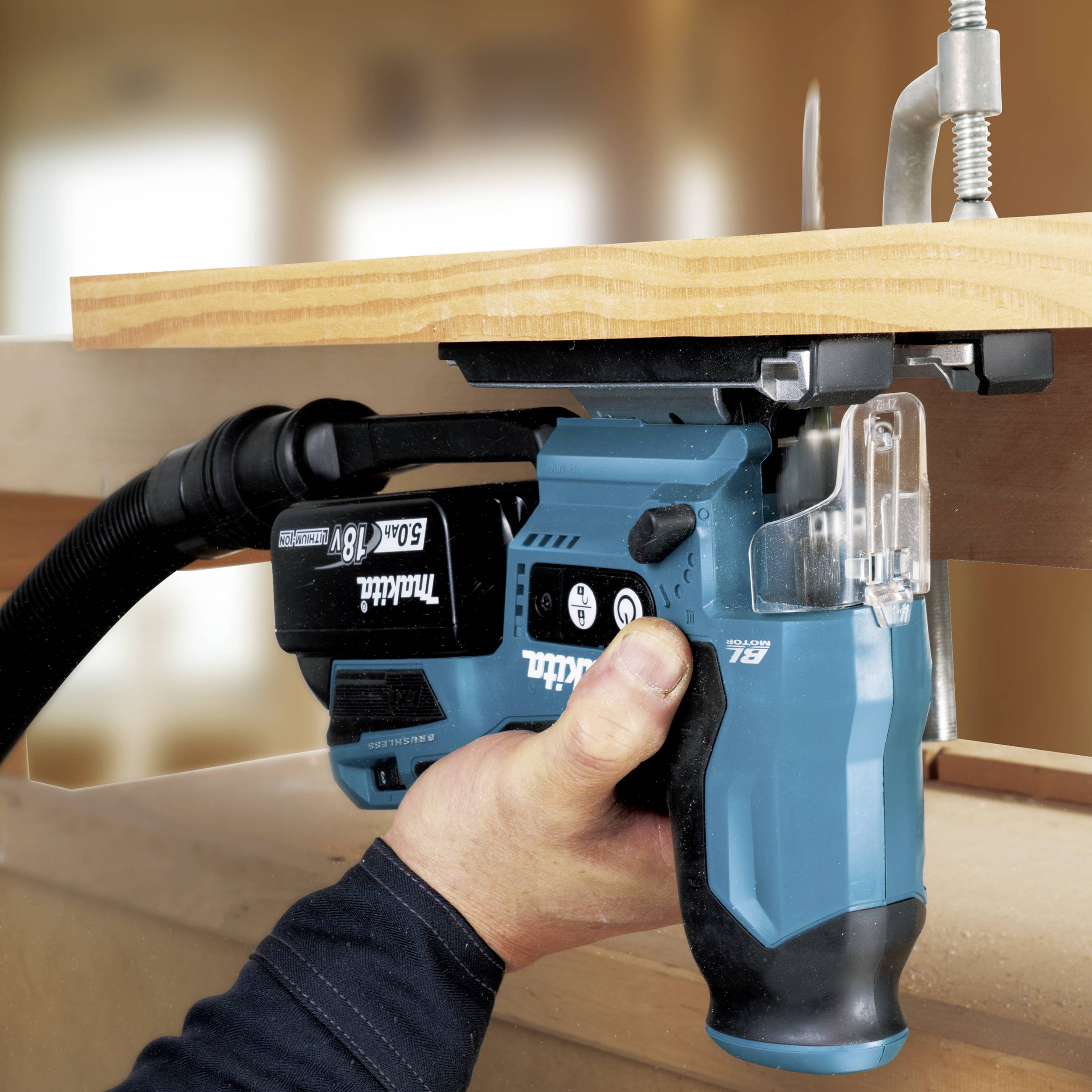 Eine elektrische Säge schneidet durch ein Holzbrett. Eine Hand hält das Werkzeug. Ein Staubsaugeraufsatz entfernt den Staub.