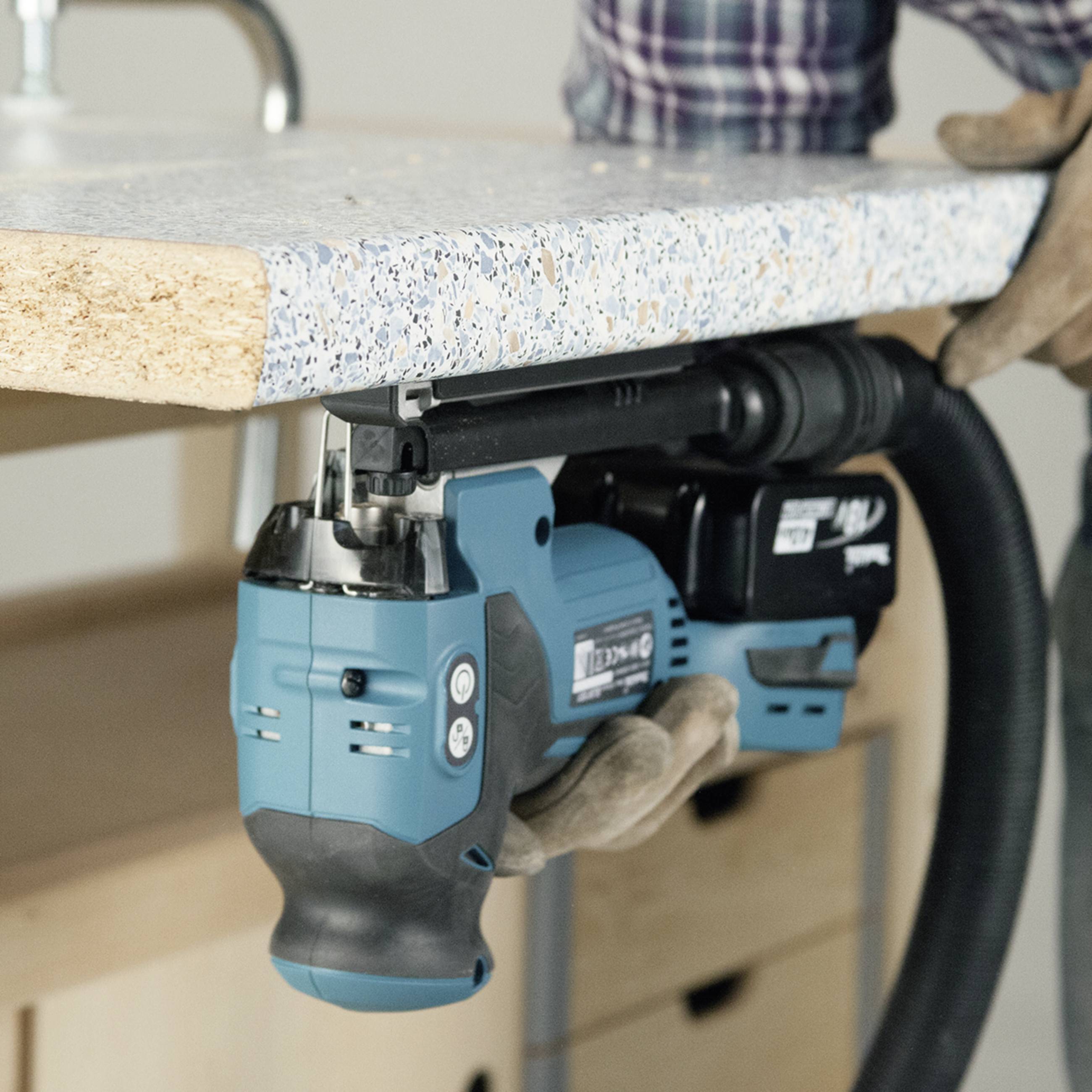 Eine Person verwendet ein Elektrowerkzeug, um ein großes, rechteckiges Stück Material auf einer Werkbank zu bearbeiten.