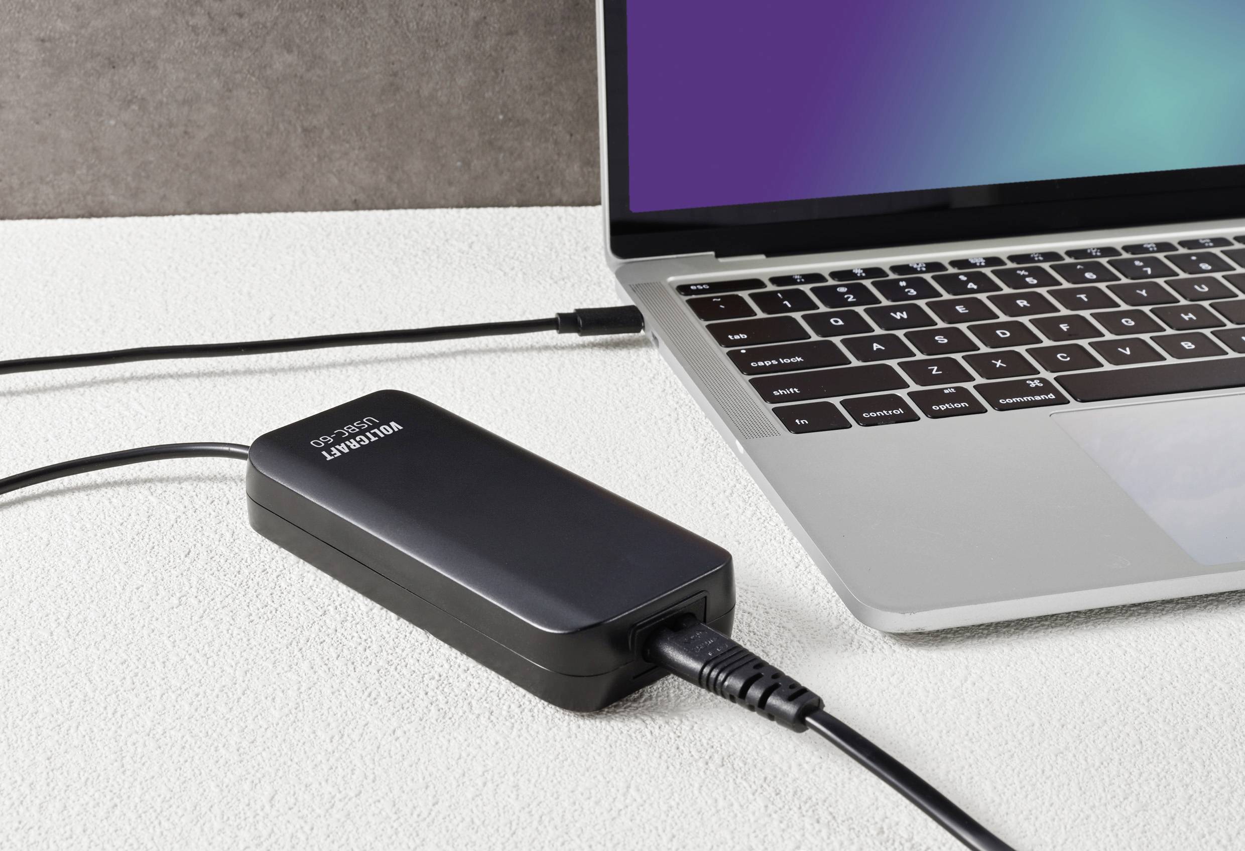 Ein Laptop ist mit einem tragbaren Ladegerät verbunden, das auf einem Tisch liegt. Der Bildschirm des Laptops ist teilweise sichtbar.