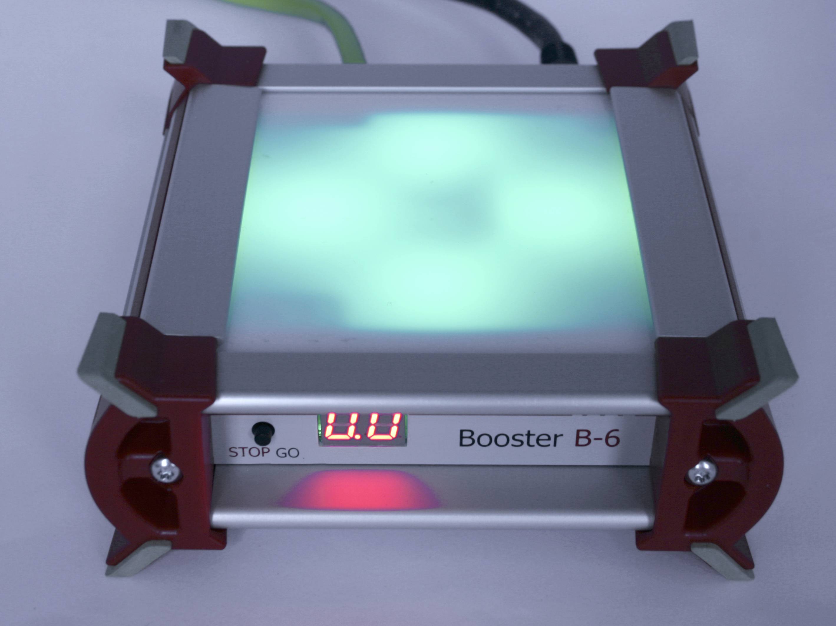 Ein quadratisches Gerät mit der Aufschrift 'Booster B-6'. Eine digitale Anzeige zeigt '0.0'. Ein leuchtendes grünes Licht ist zu sehen.