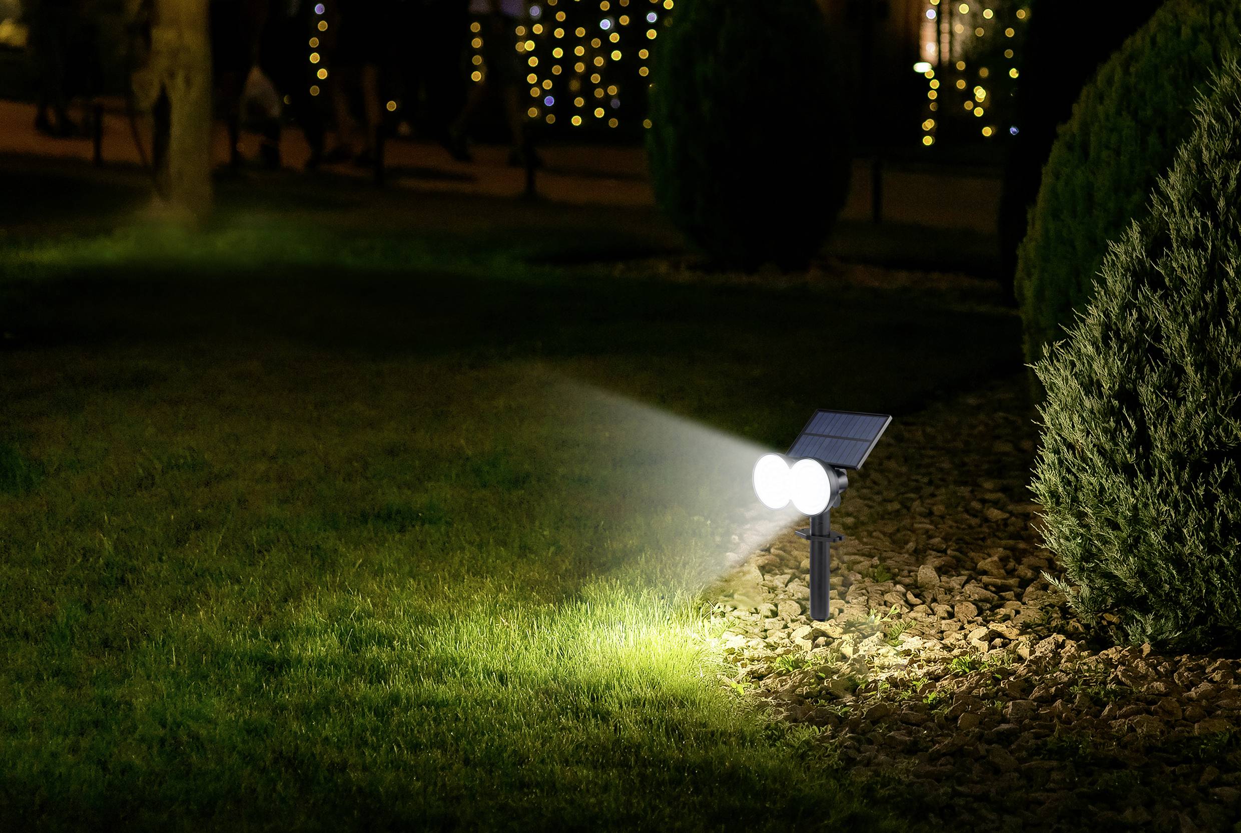 Eine Solarlampe beleuchtet nachts einen Gartenweg. Im Hintergrund sind Bäume und verschwommene Lichter zu sehen.