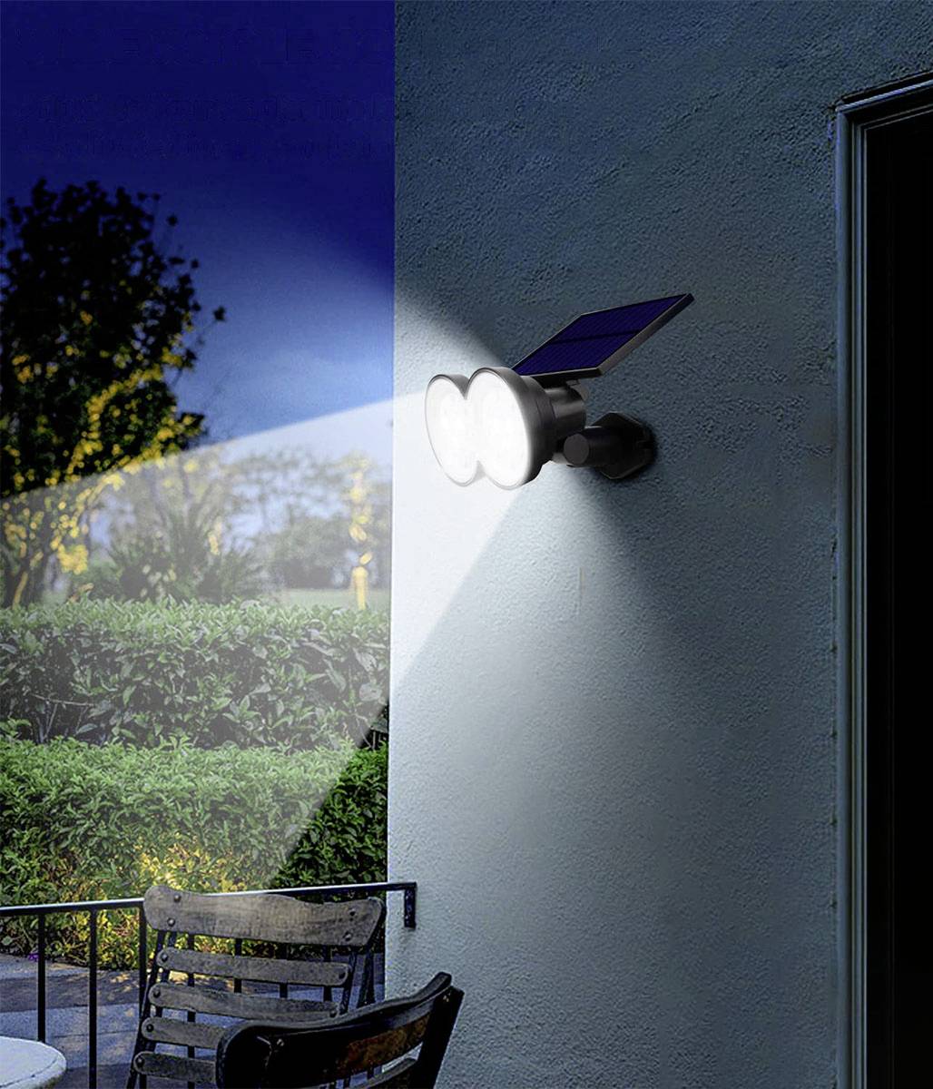 Solarbetriebene Außenwandleuchte mit Doppelstrahlern, die in der Dunkelheit einen Gartenbereich beleuchtet.