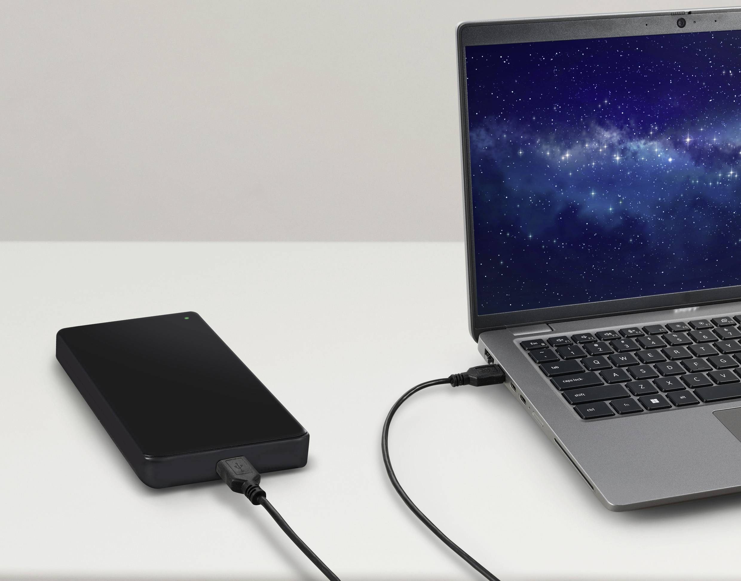 Externe Festplatte ist über ein USB-Kabel mit einem Laptop verbunden. Auf dem Laptopbildschirm ist ein Nachthimmel zu sehen.