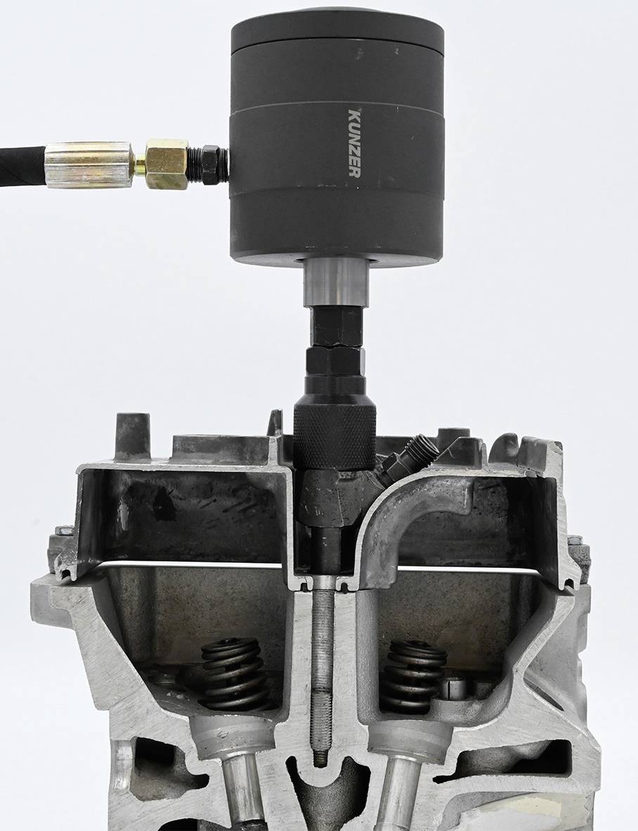 Ein Werkzeug zur Überprüfung der Zylinderkompression ist mit einem offenen Motorzylinder verbunden. Adapter und Federn sichtbar.