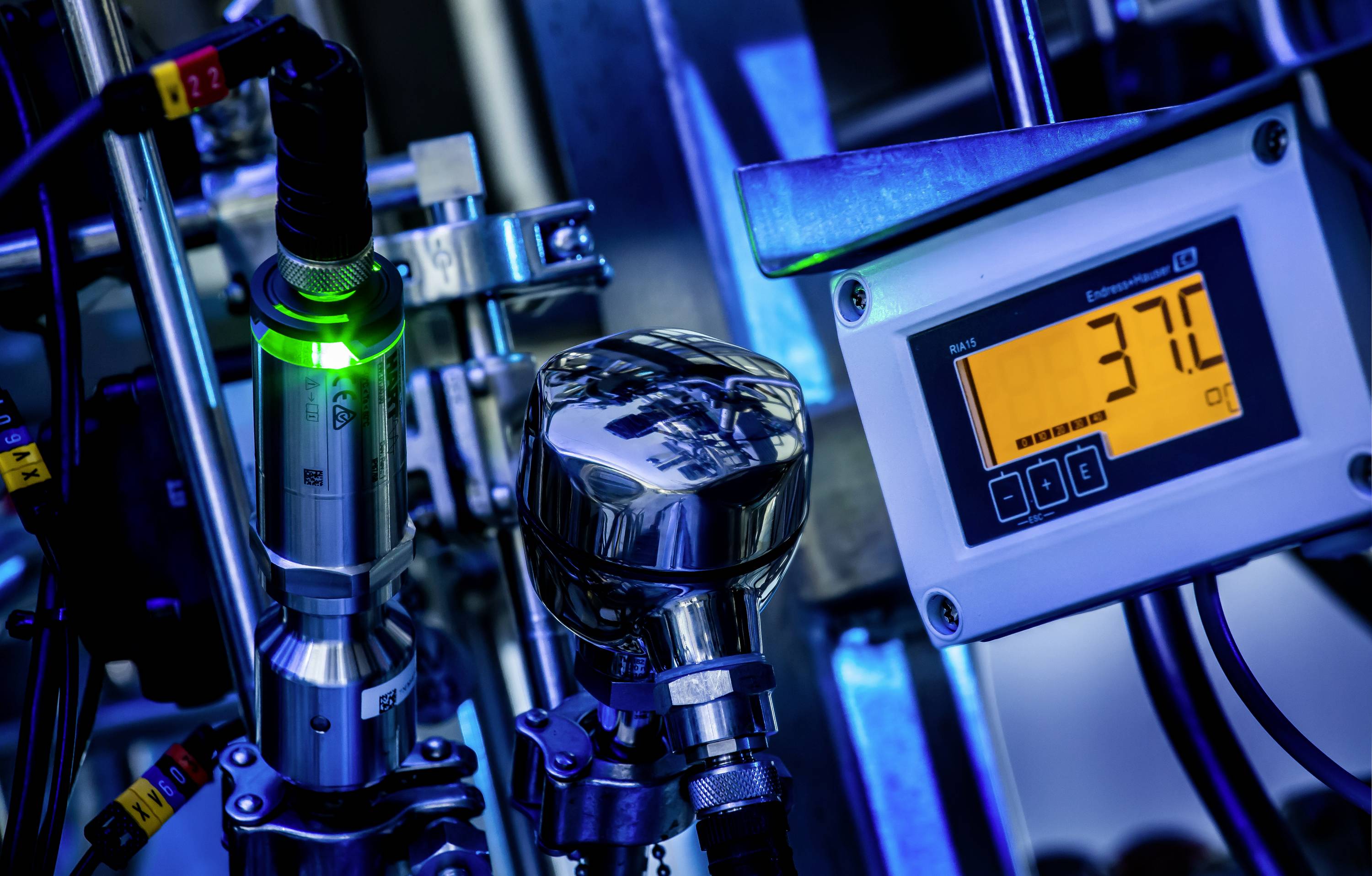 Industrieszene mit Metallrohren und einem Display, das '37.0' anzeigt. Anzeige der Temperatur in einem technischen Prozess.