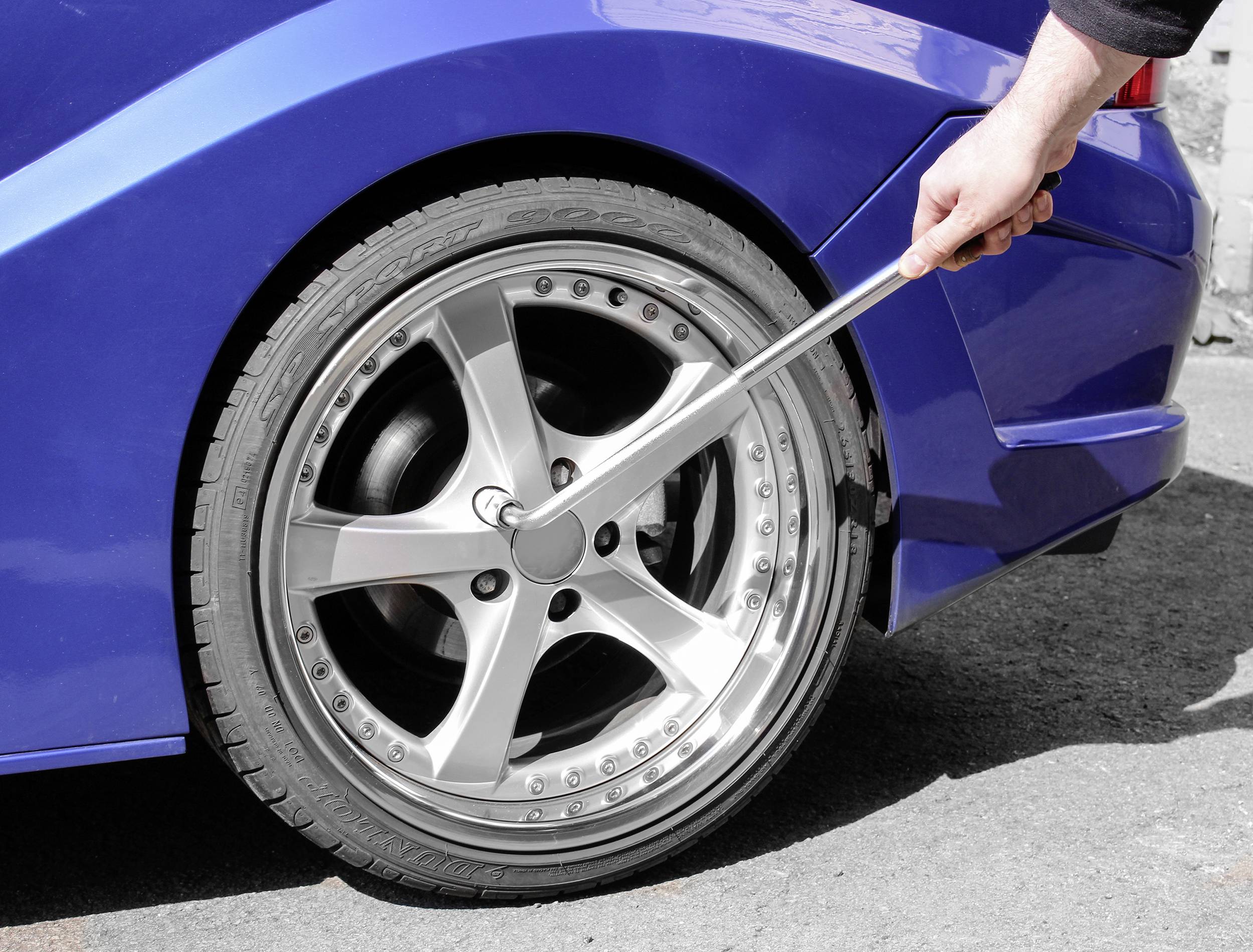 Eine Person zieht mit einem großen Schraubenschlüssel die Muttern an einem Autoreifen fest. Der Wagen ist blau.