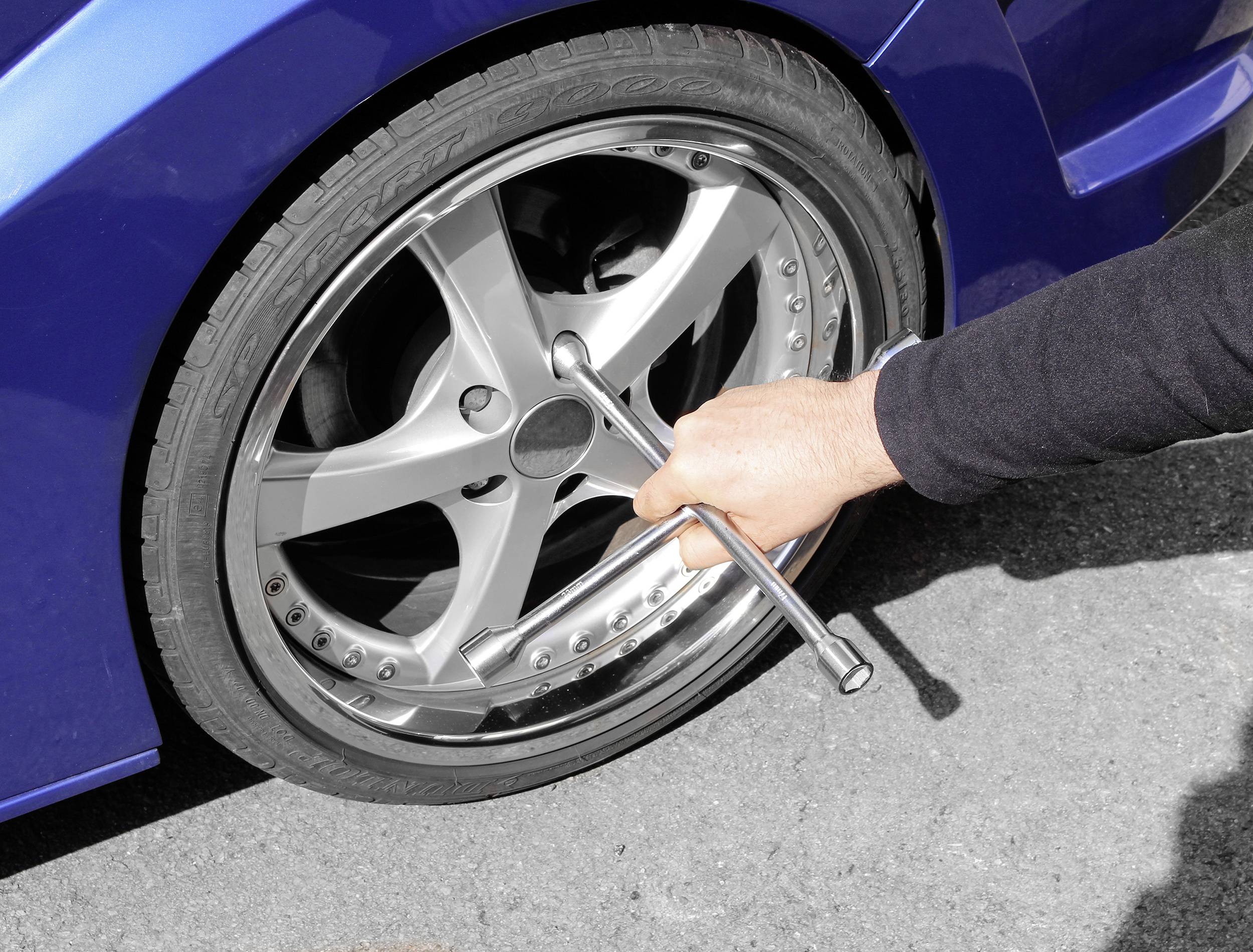 Eine Person wechselt ein Autoreifen und zieht die Radmuttern mit einem Kreuzschlüssel an. Das Auto hat eine blaue Karosserie.