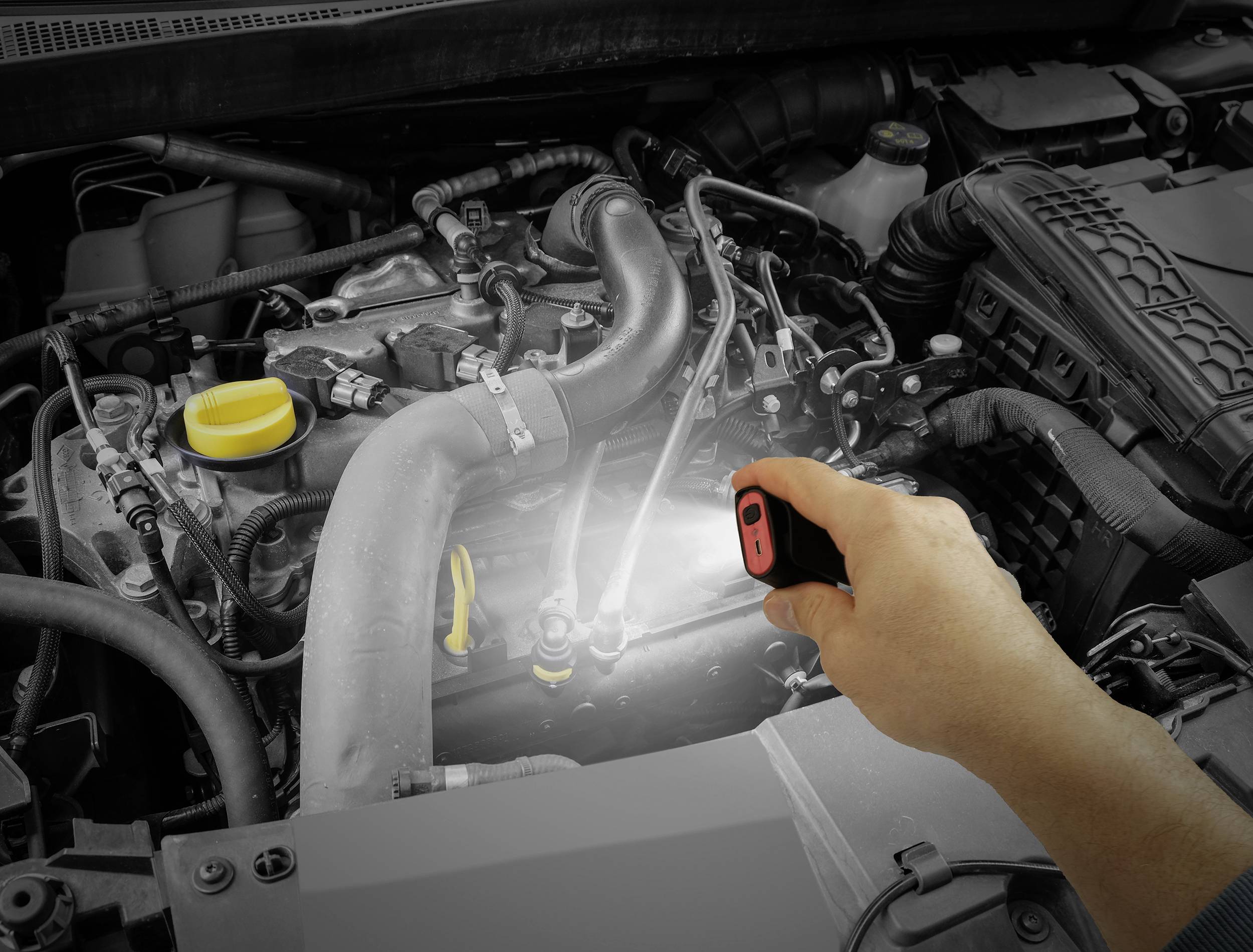 Eine Person beleuchtet mit einer Taschenlampe den Motor eines Autos, um Details der Motorkomponenten anzusehen.