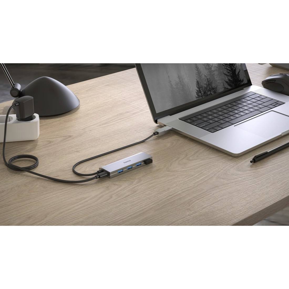 Notebook auf einem Tisch, verbunden mit einer Dockingstation über ein Kabel. Nebenbei ein Stift, Lampe und Steckdose im Hintergrund.