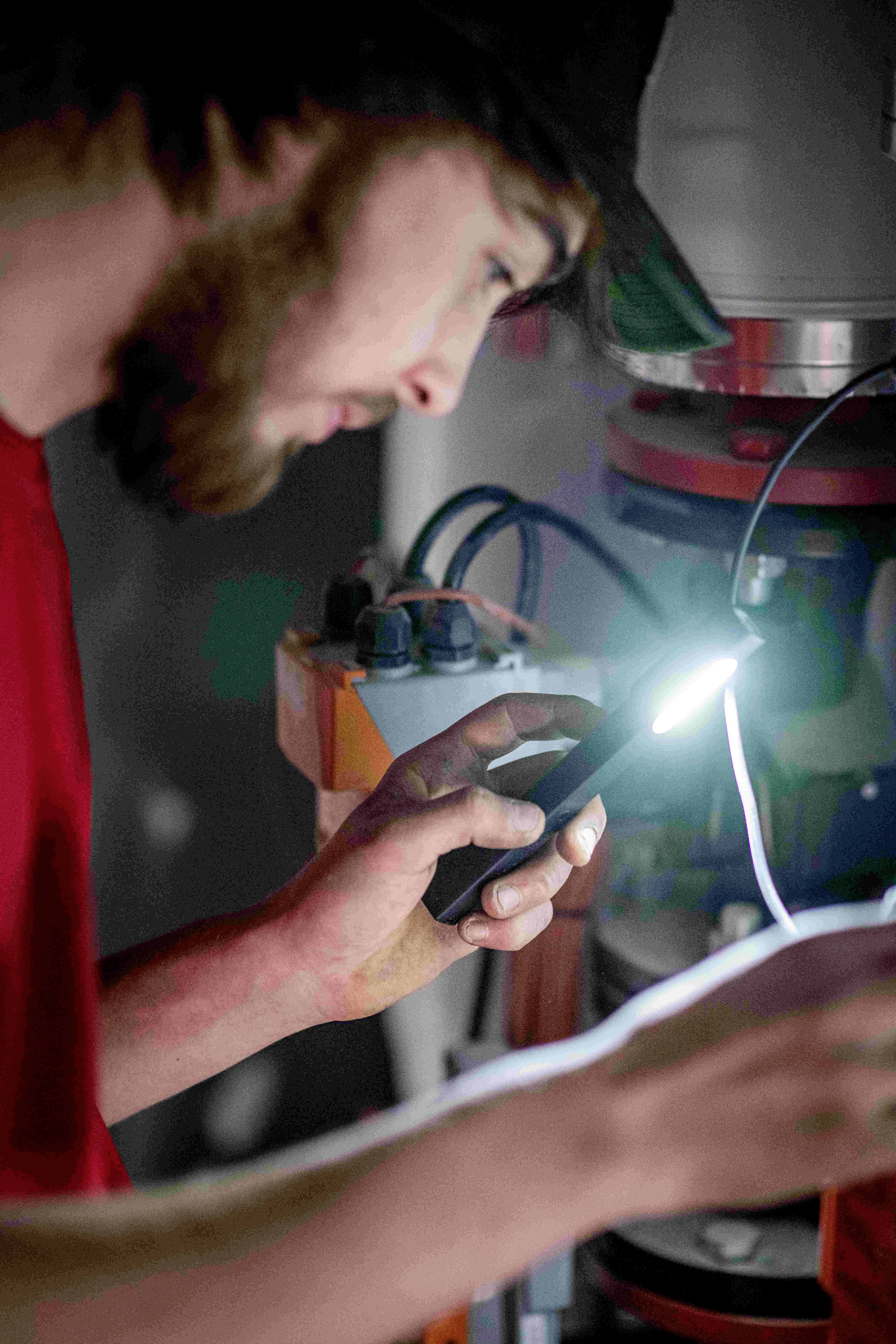 Ein Mann benutzt eine Taschenlampe zur Inspektion von elektrischen Komponenten in einem Gerät. Er konzentriert sich auf seine Arbeit.