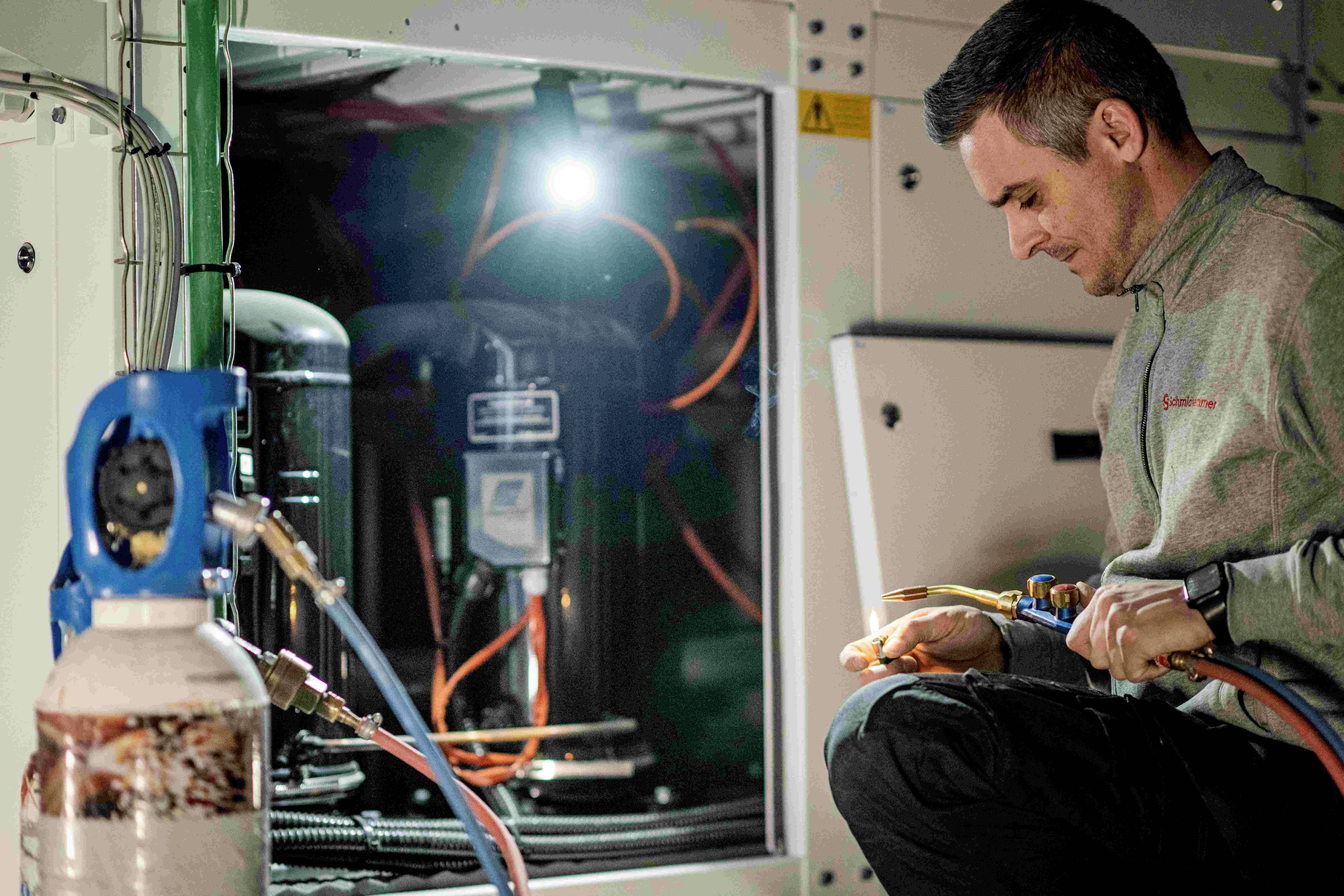 Ein Techniker arbeitet konzentriert mit Werkzeugen an einer Maschine im Inneren eines Technikraums, beleuchtet von einer Lampe.