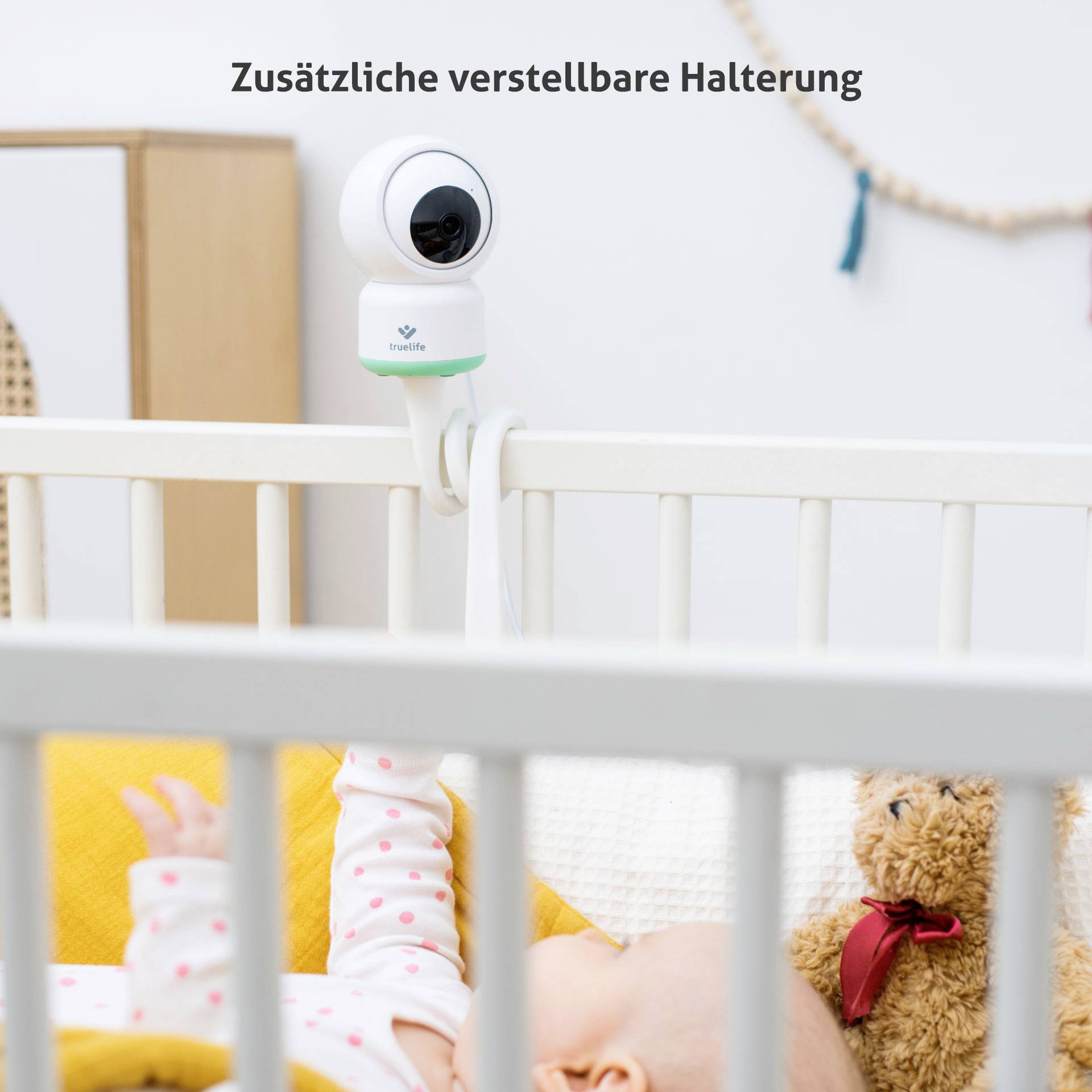 Babyphone-Kamera mit verstellbarer Halterung an einem Kinderbett montiert. Schlafendes Baby im Vordergrund.