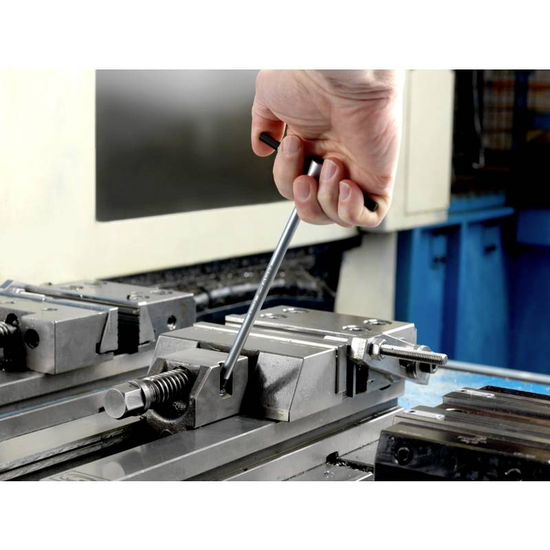 Eine Hand spannt ein Werkstück mit einem Schraubenschlüssel in einem Maschinenschraubstock fest, bereit für den Bearbeitungsprozess.