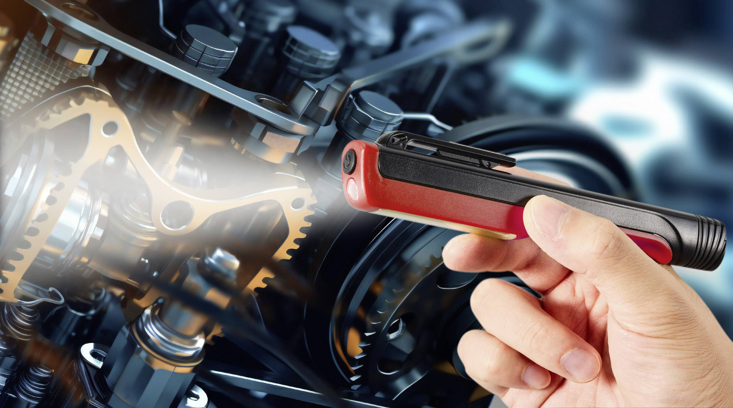 Eine Person hält ein rot-schwarzes Gerät, das auf Teile eines komplexen Maschinenmotors oder mechanischen Systems gerichtet ist.